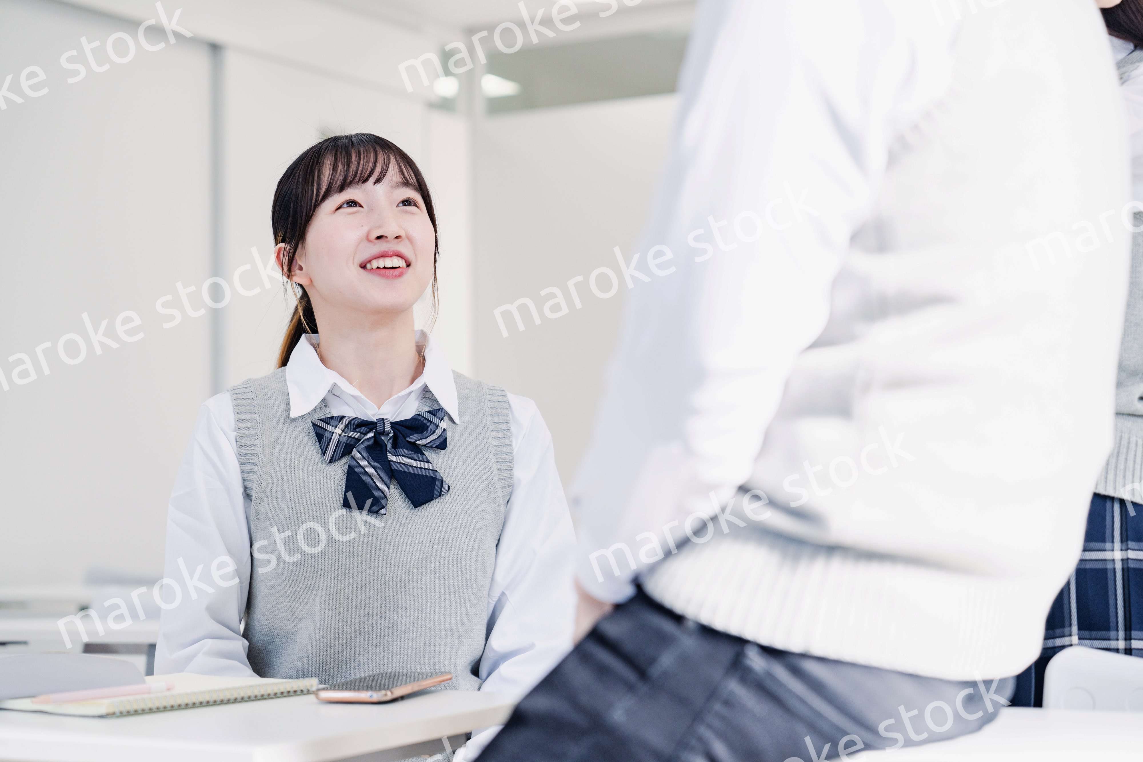 教室でクラスメイトと雑談をする高校生