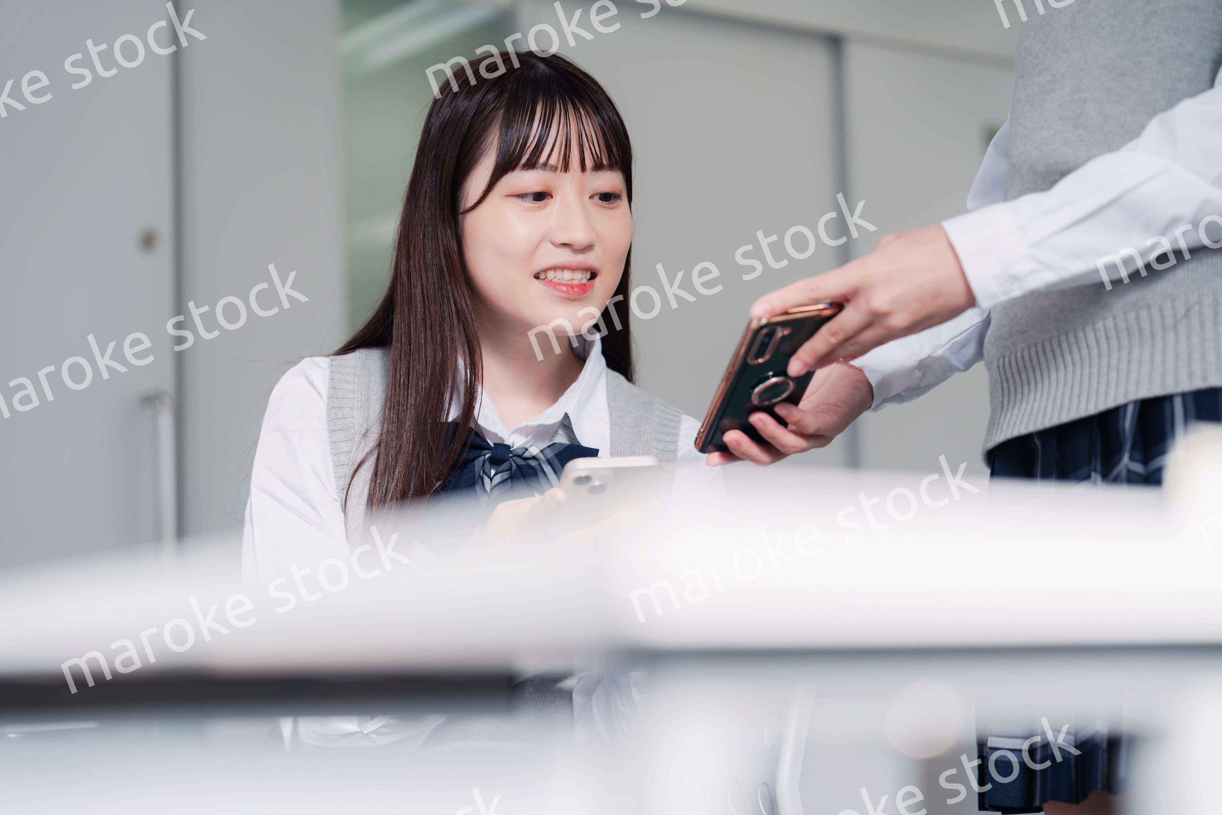 教室でスマホを見ながら話す女子高生