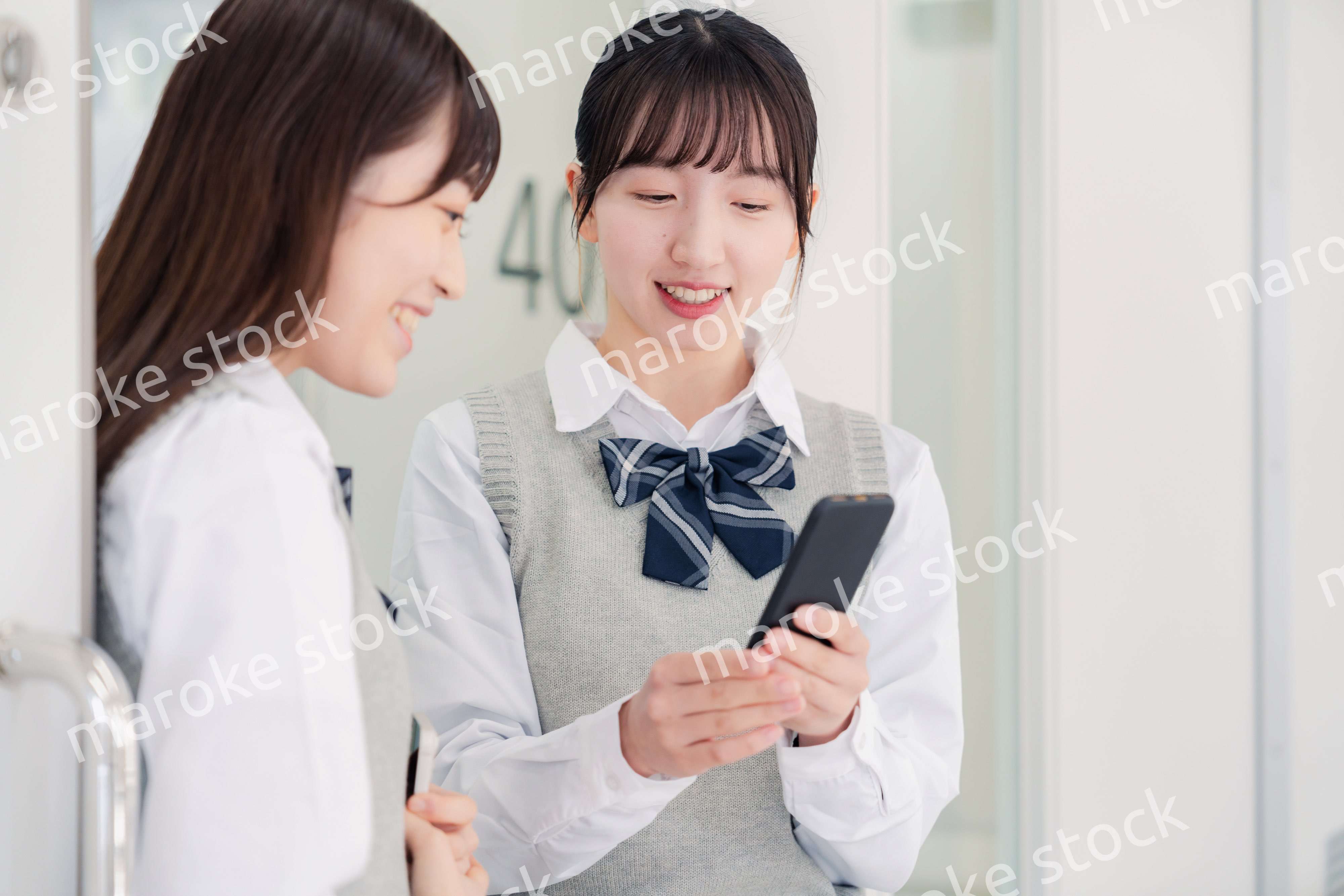 教室でスマホを見ながら話す女子高生