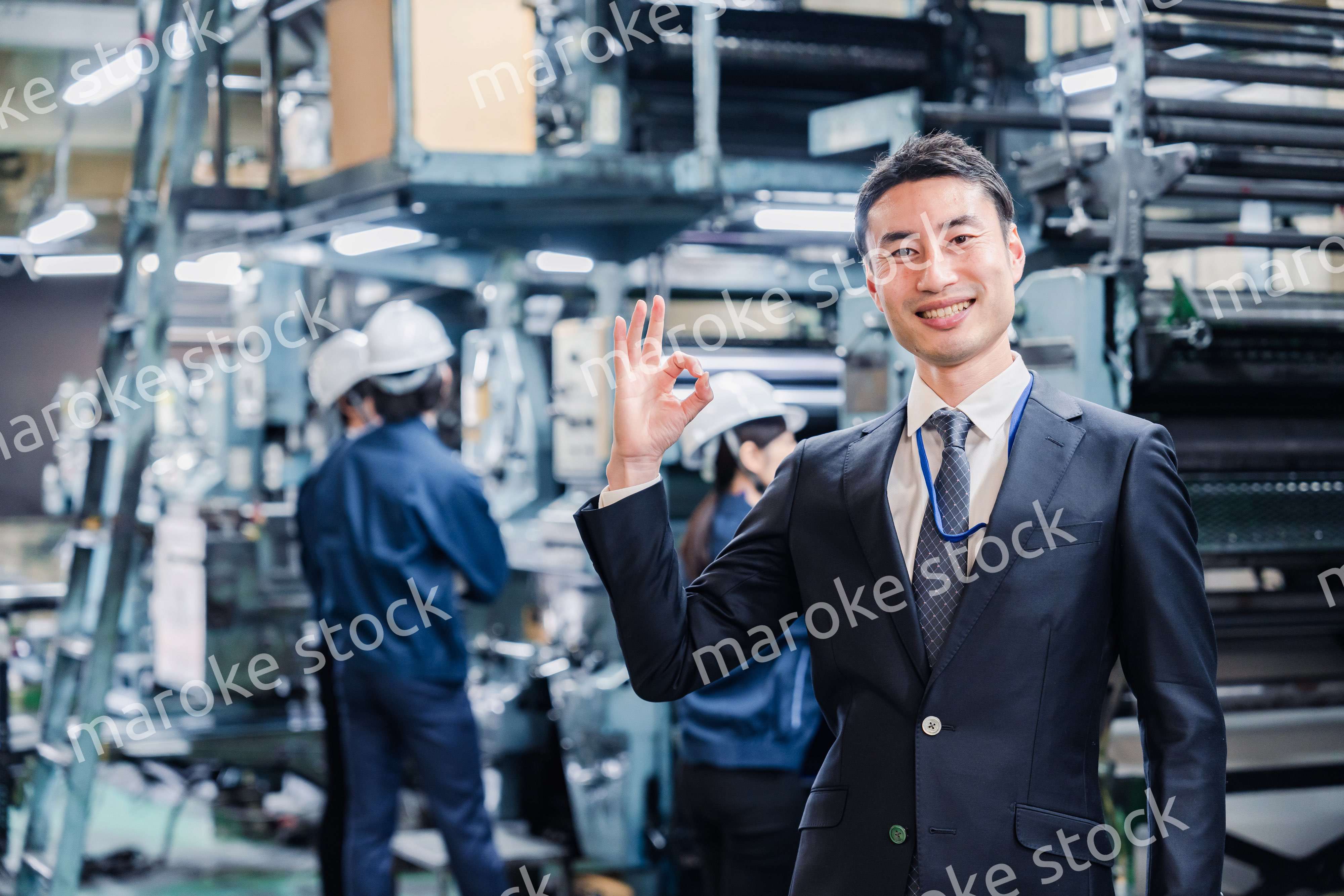 工場でOKサインをするビジネスマン