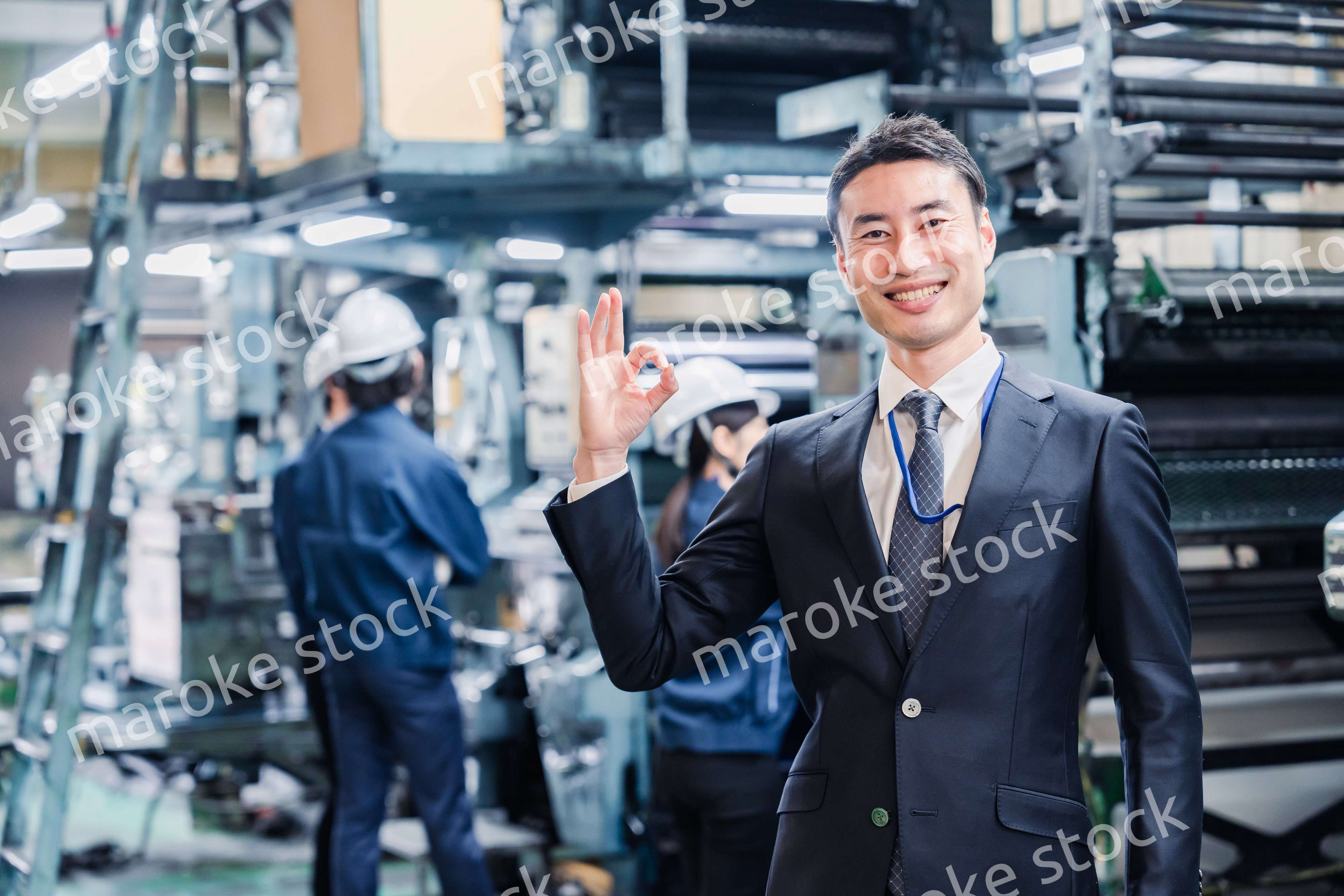 工場でOKサインをするビジネスマン