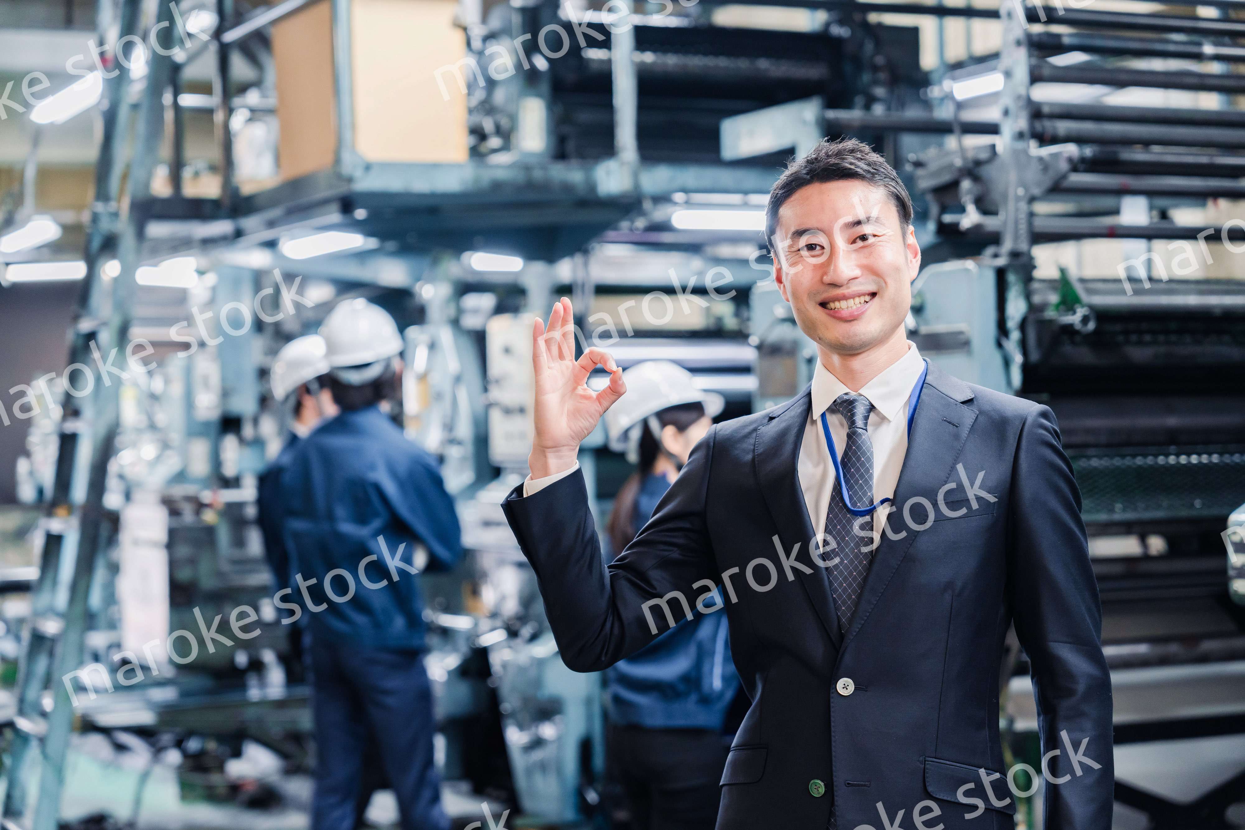 工場でOKサインをするビジネスマン