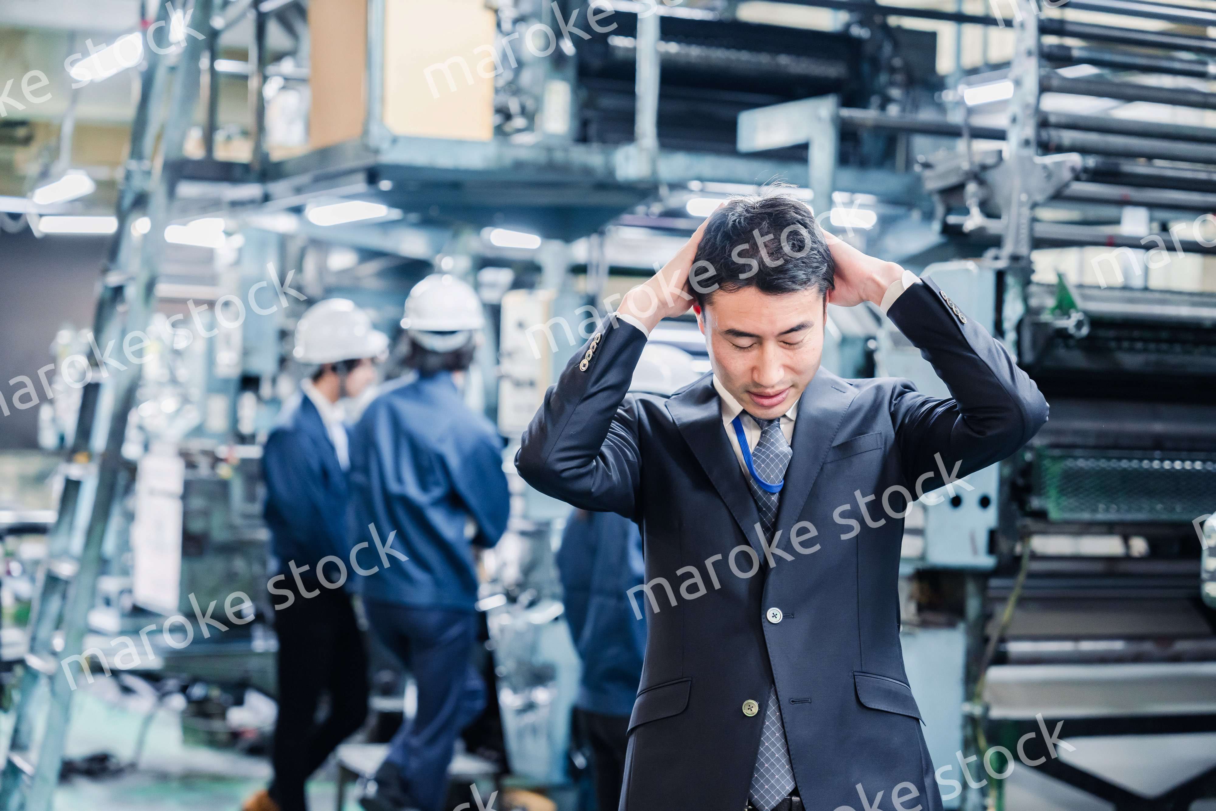 工場で頭を抱えるスーツの男性