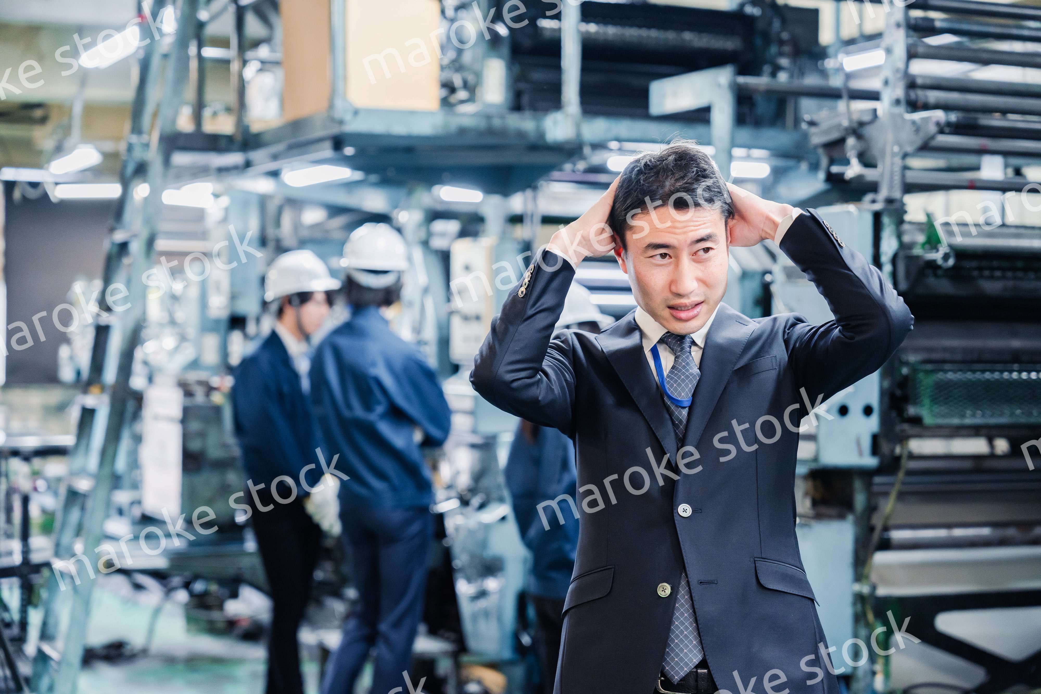 工場で頭を抱えるスーツの男性