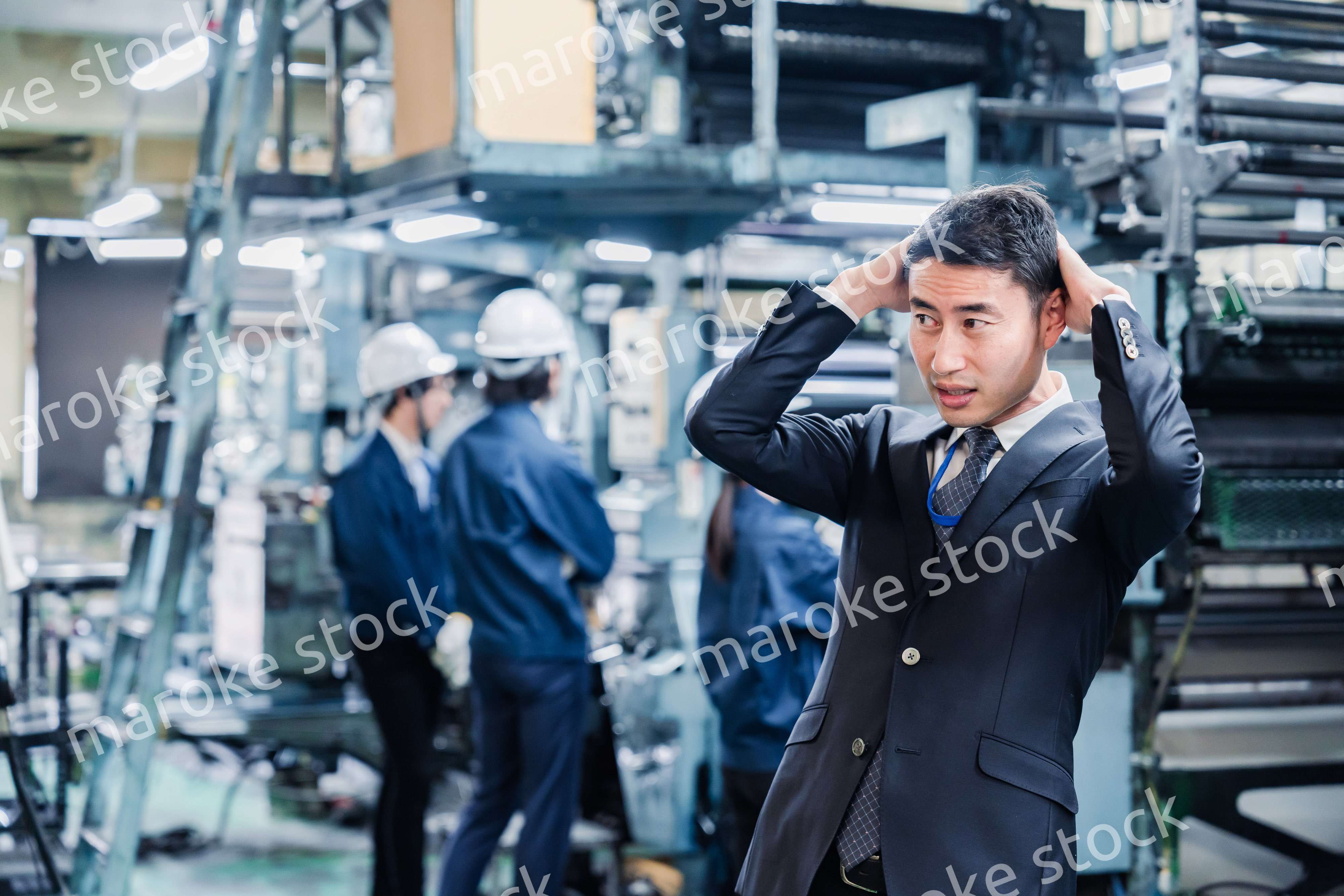工場で頭を抱えるスーツの男性