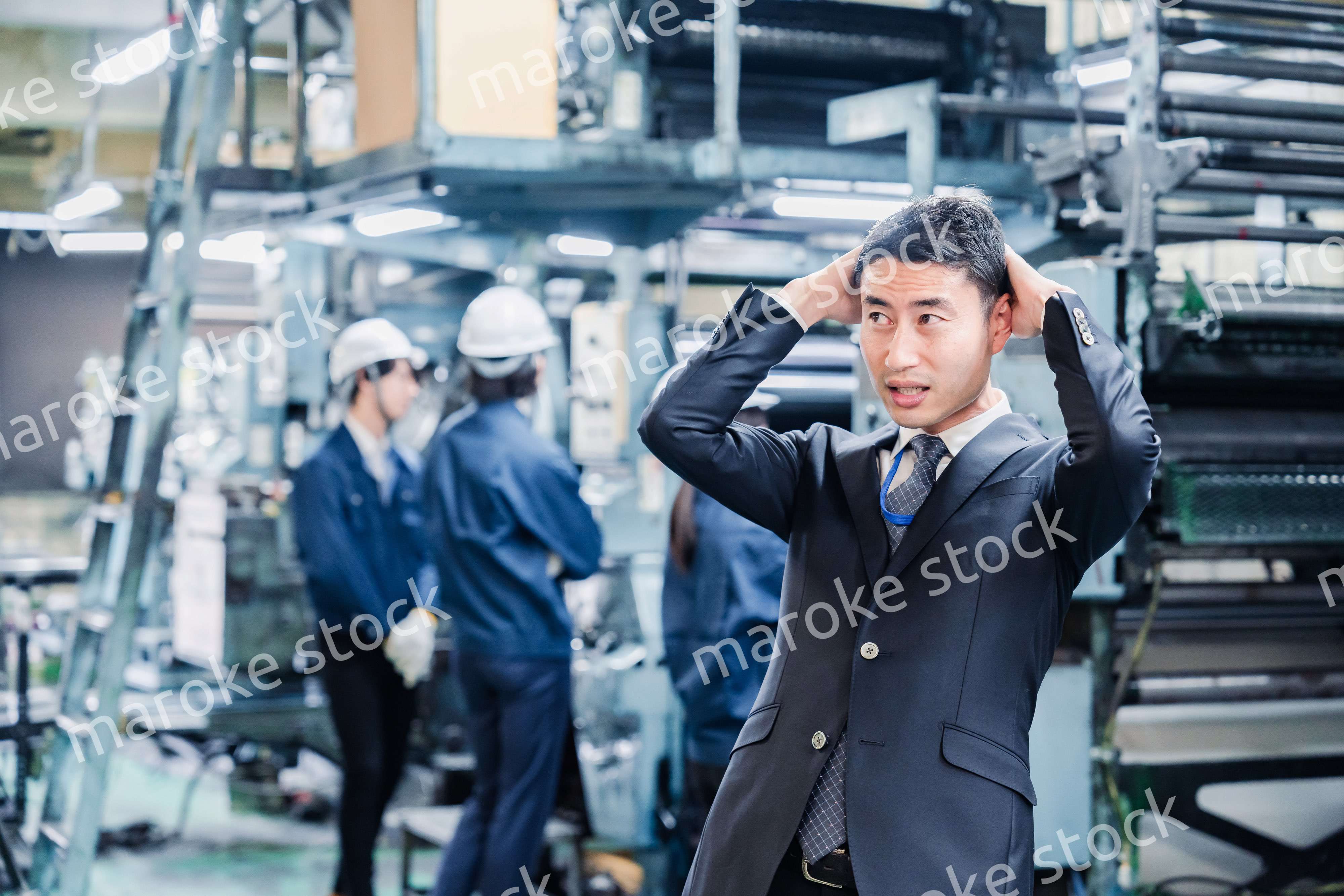 工場で頭を抱えるスーツの男性