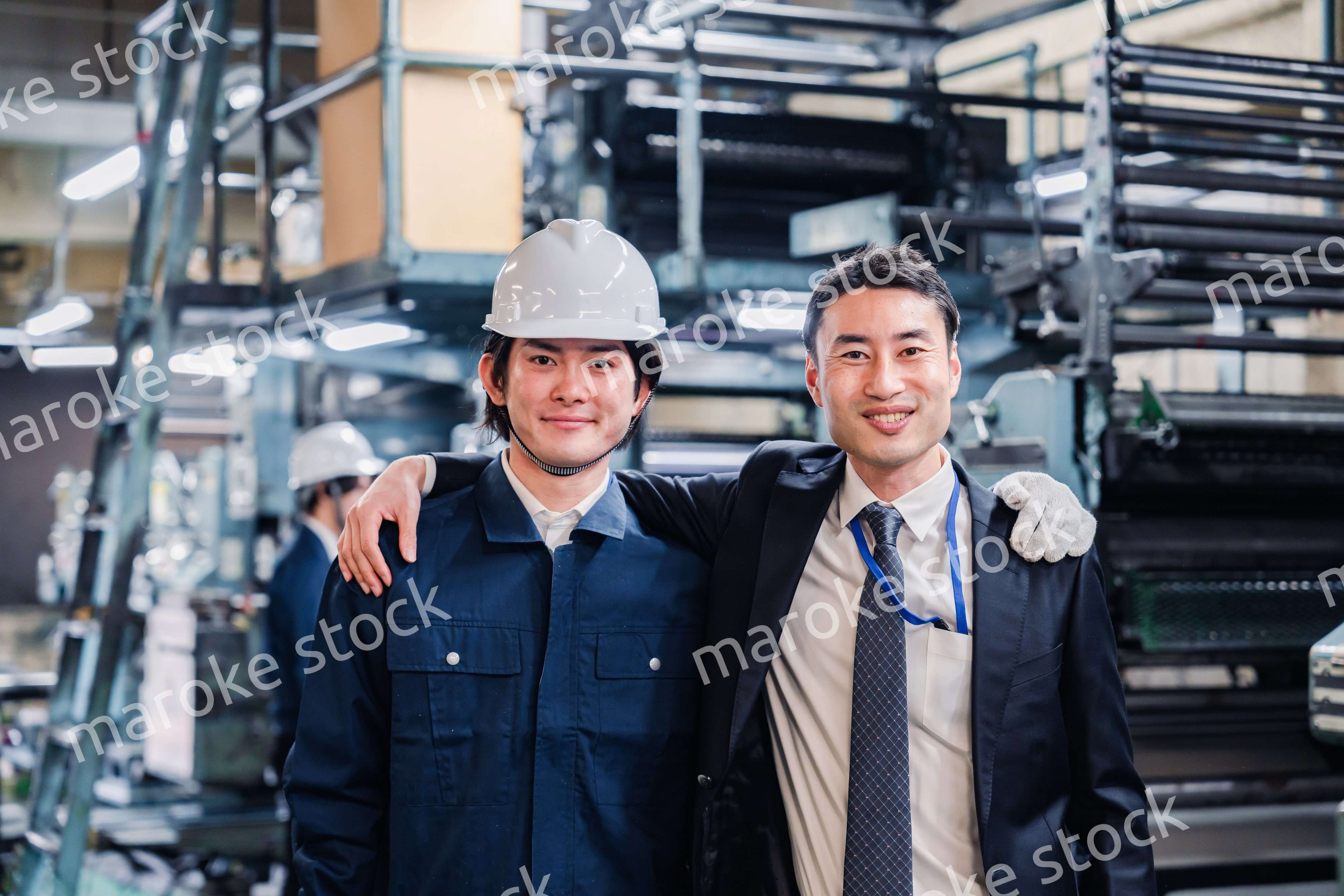 工場で肩を組む労働者と経営者