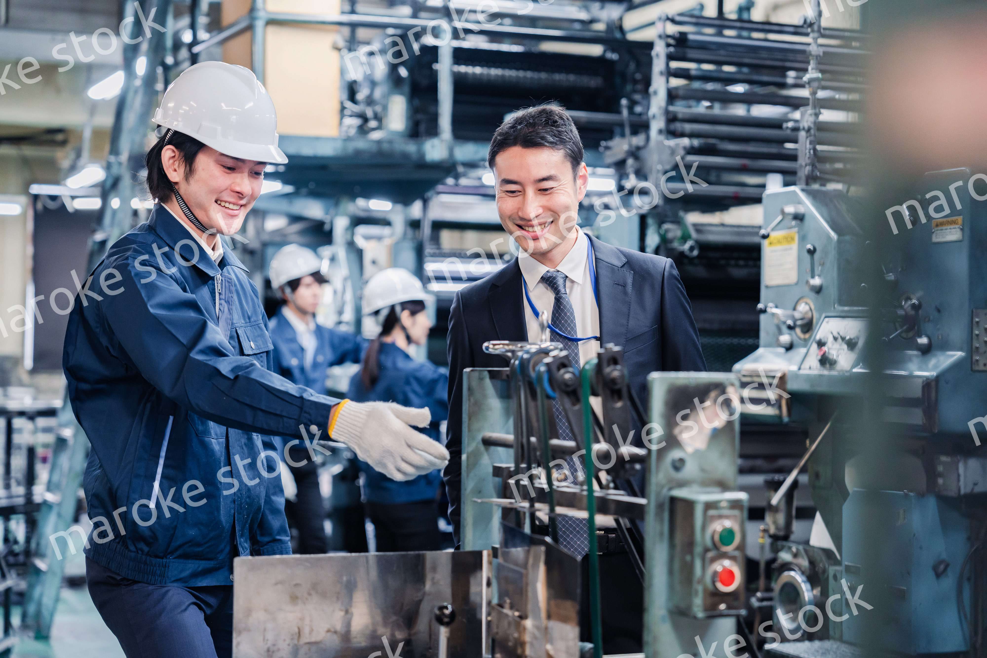 機械の前で話をする営業マンと労働者