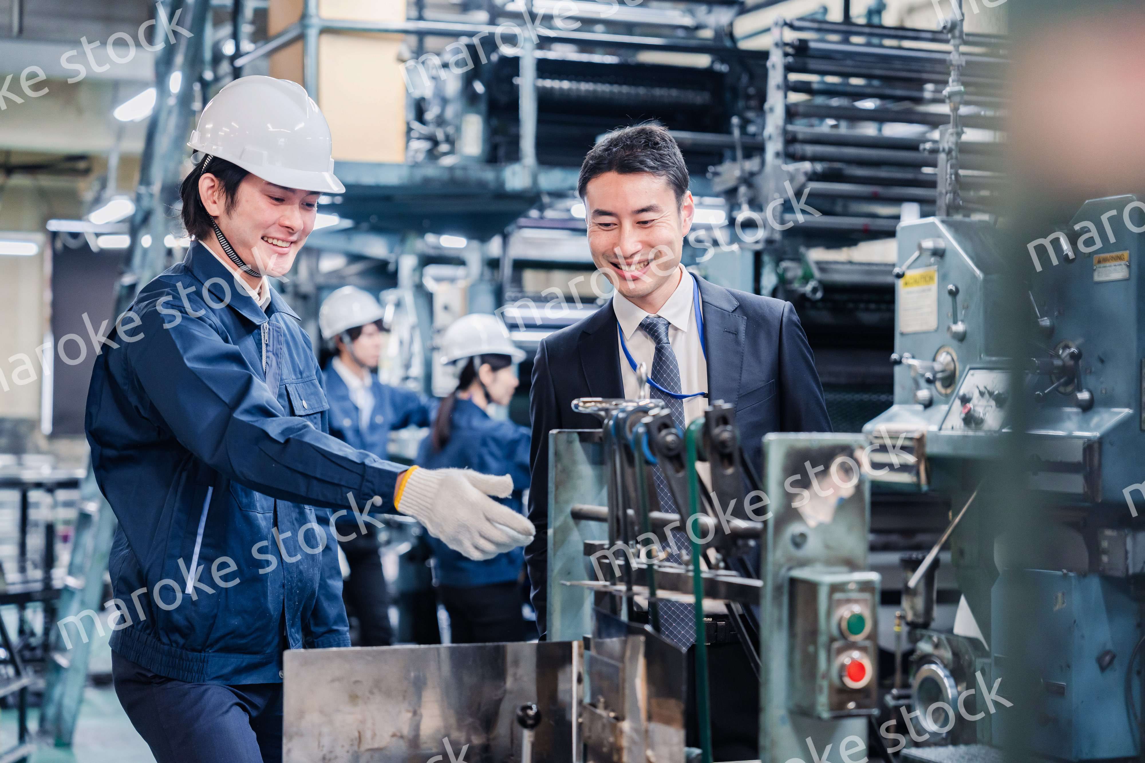 機械の前で話をする営業マンと労働者