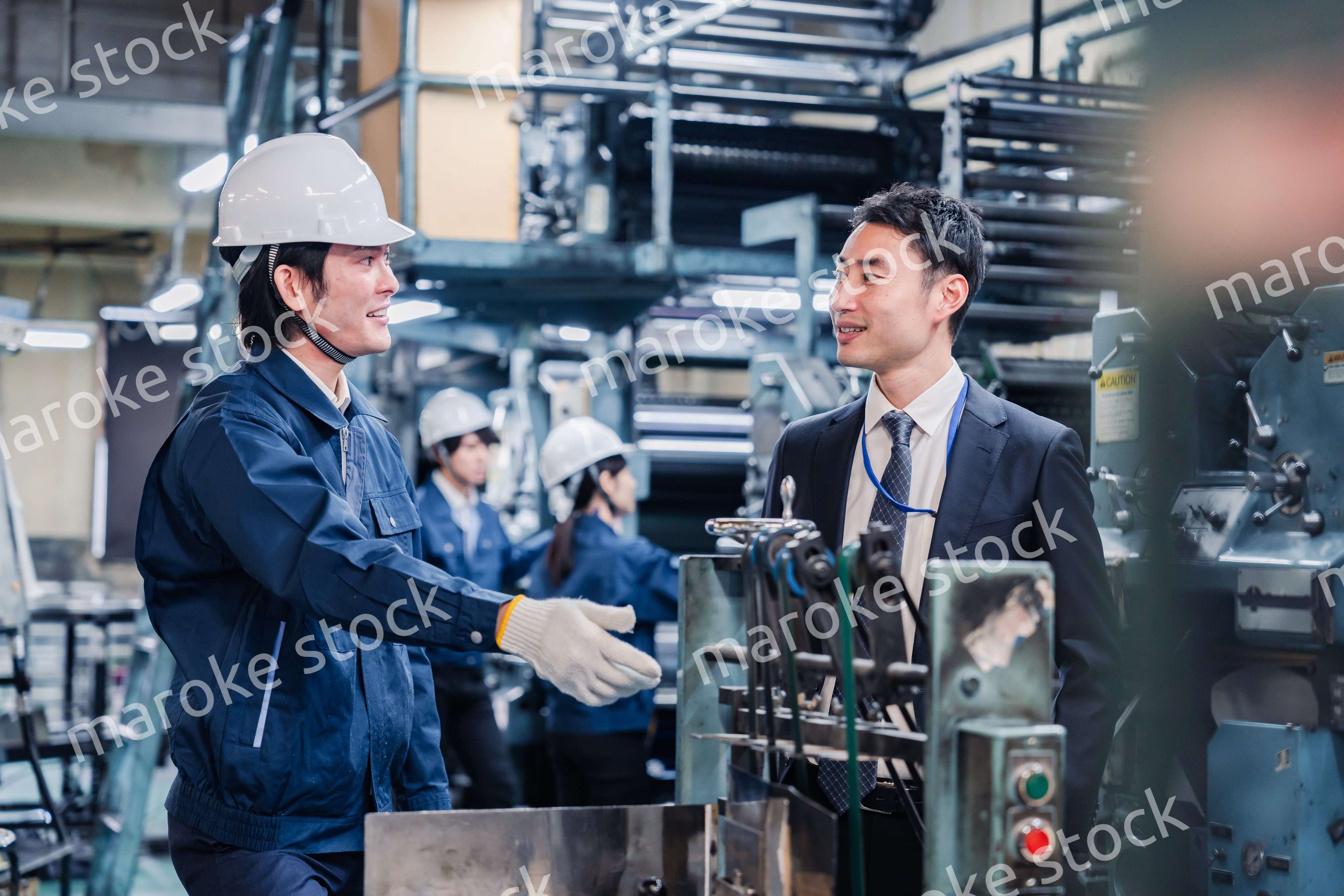 機械の前で話をする営業マンと労働者