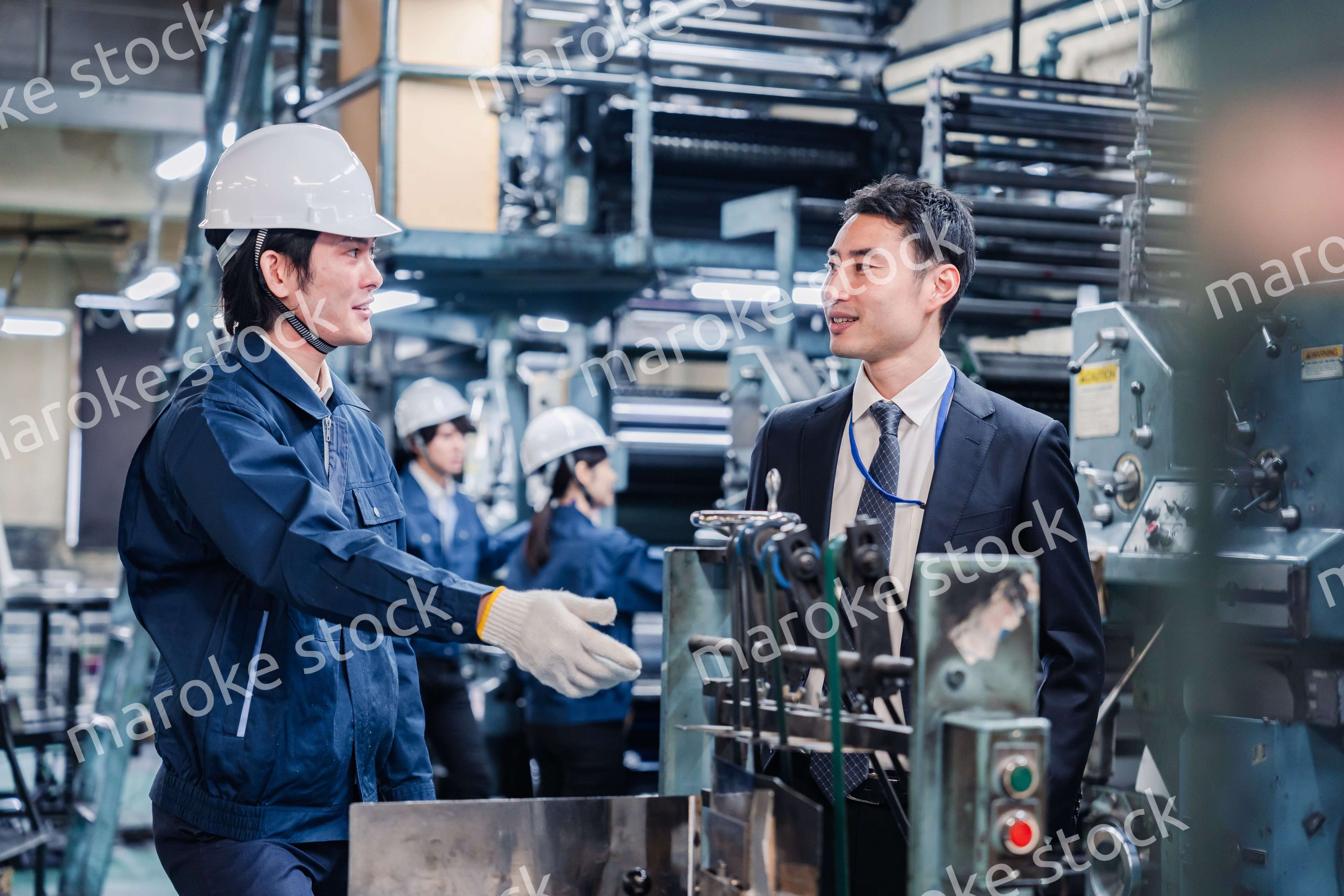 機械の前で話をする営業マンと労働者