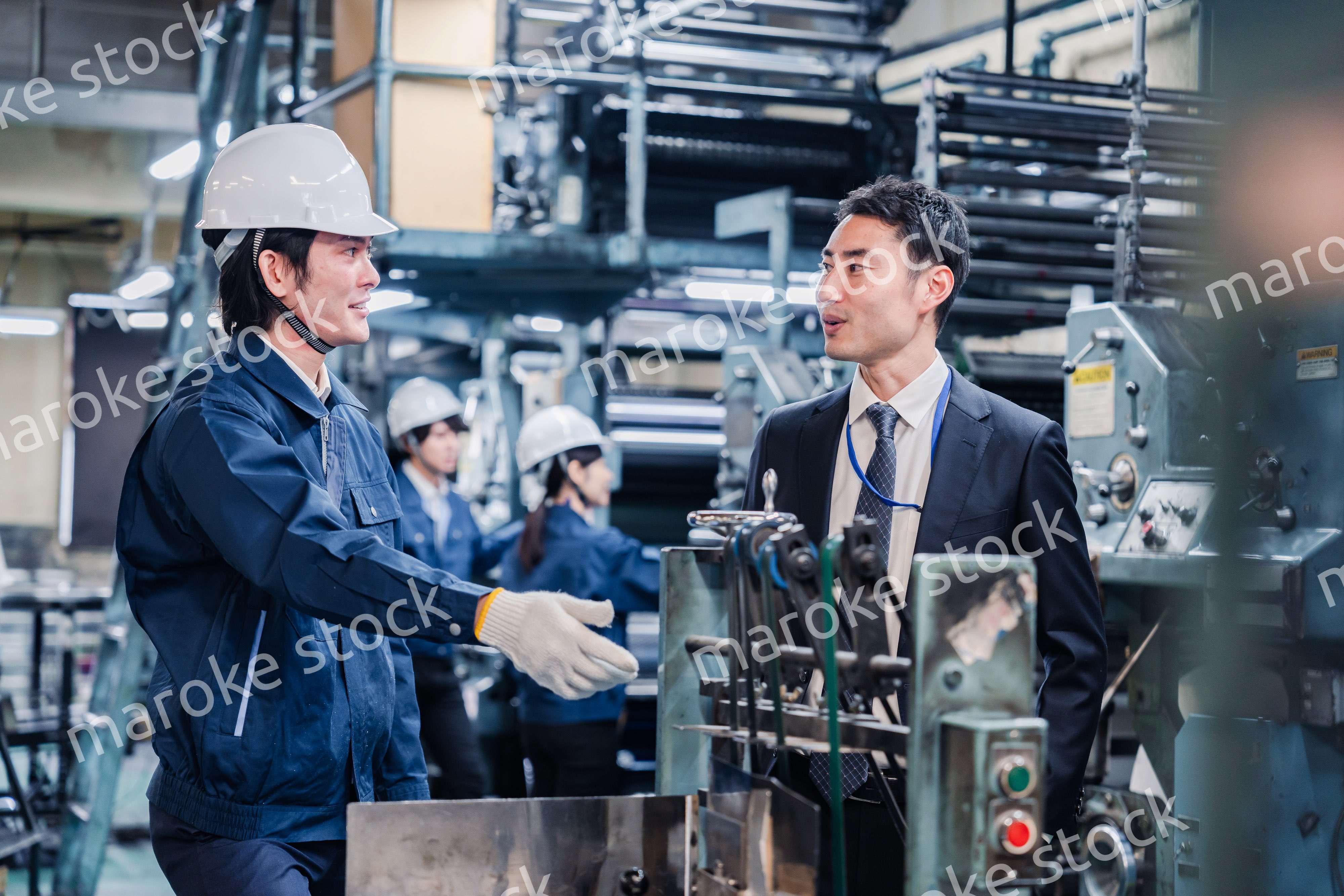 機械の前で話をする営業マンと労働者