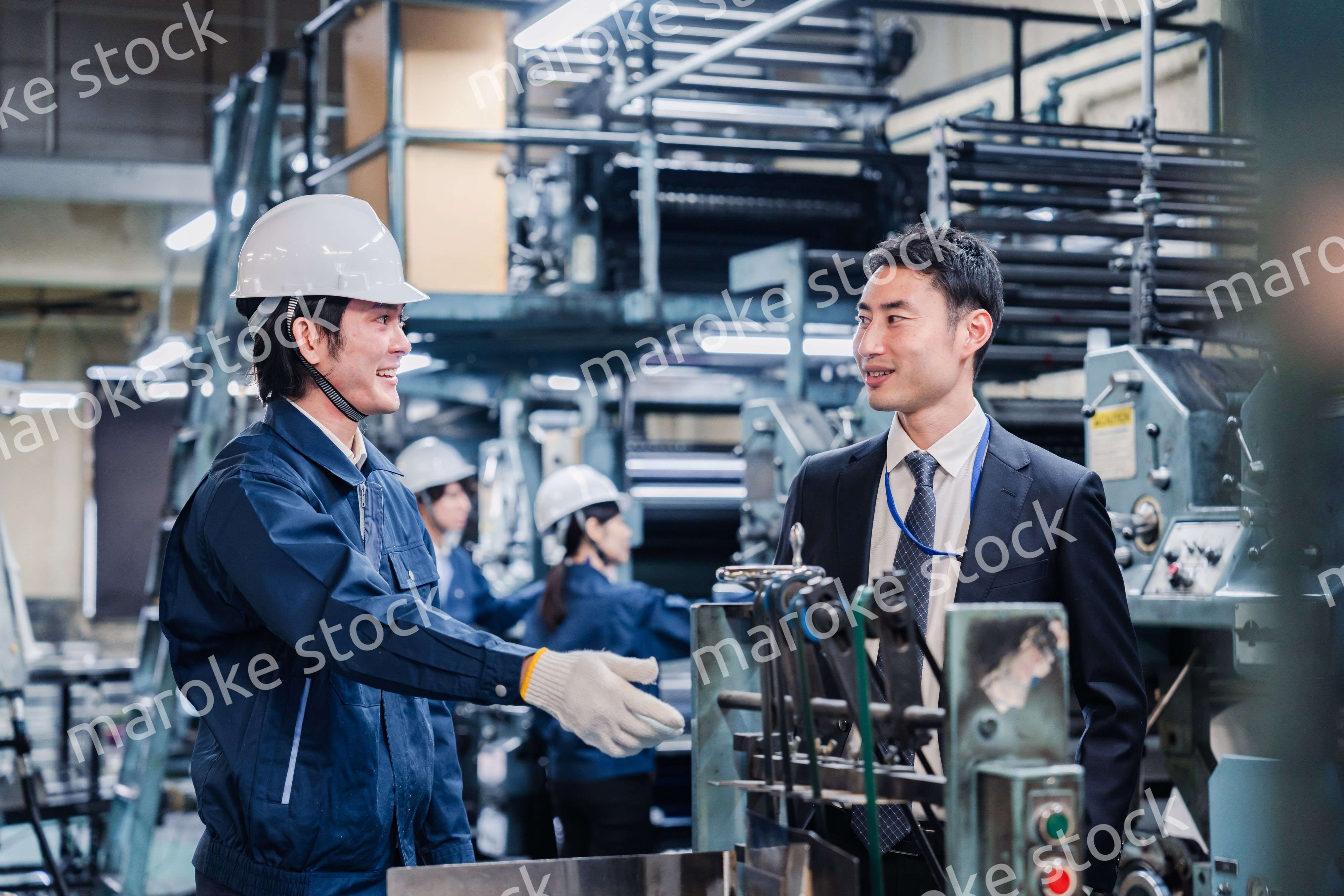 機械の前で話をする営業マンと労働者