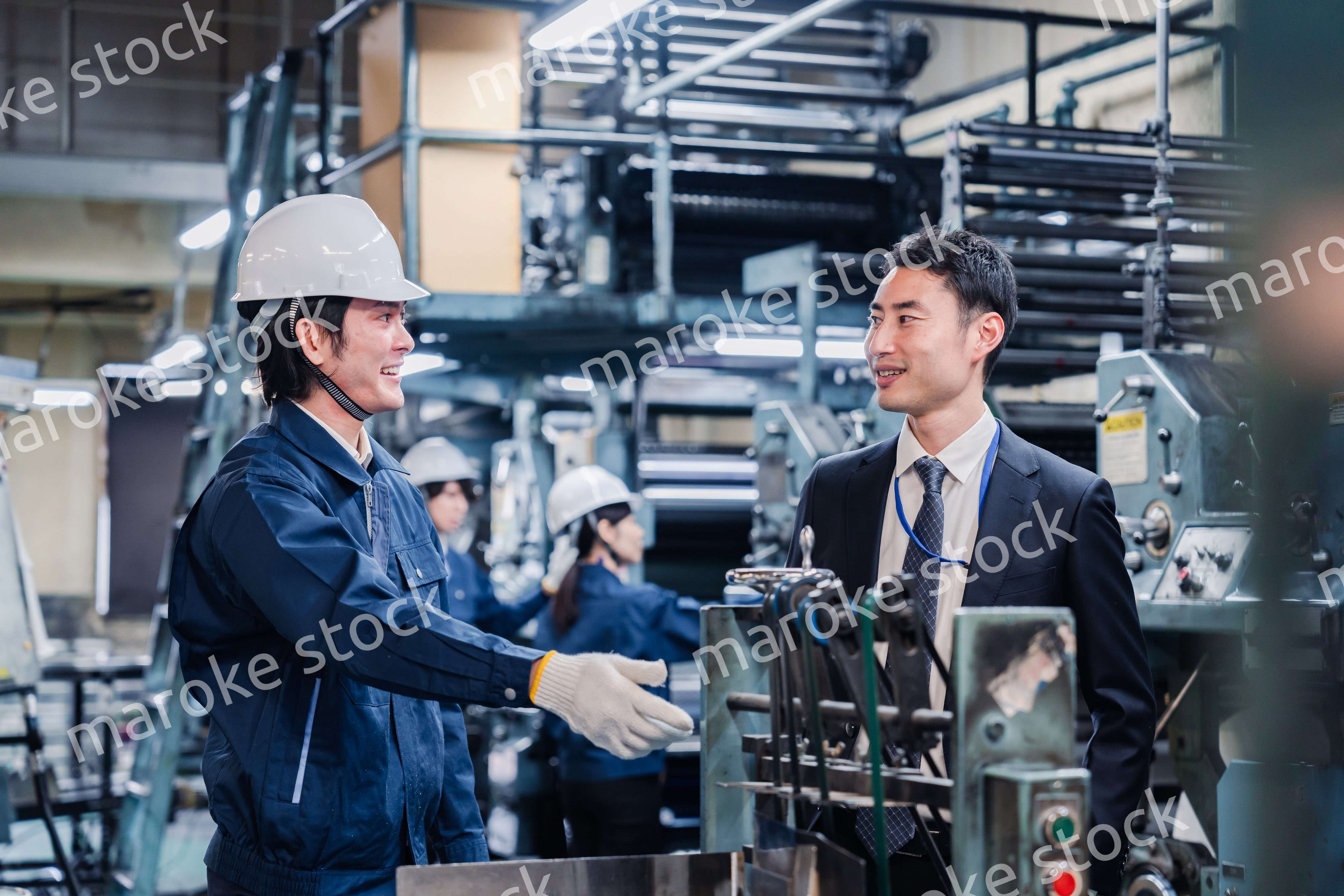 機械の前で話をする営業マンと労働者