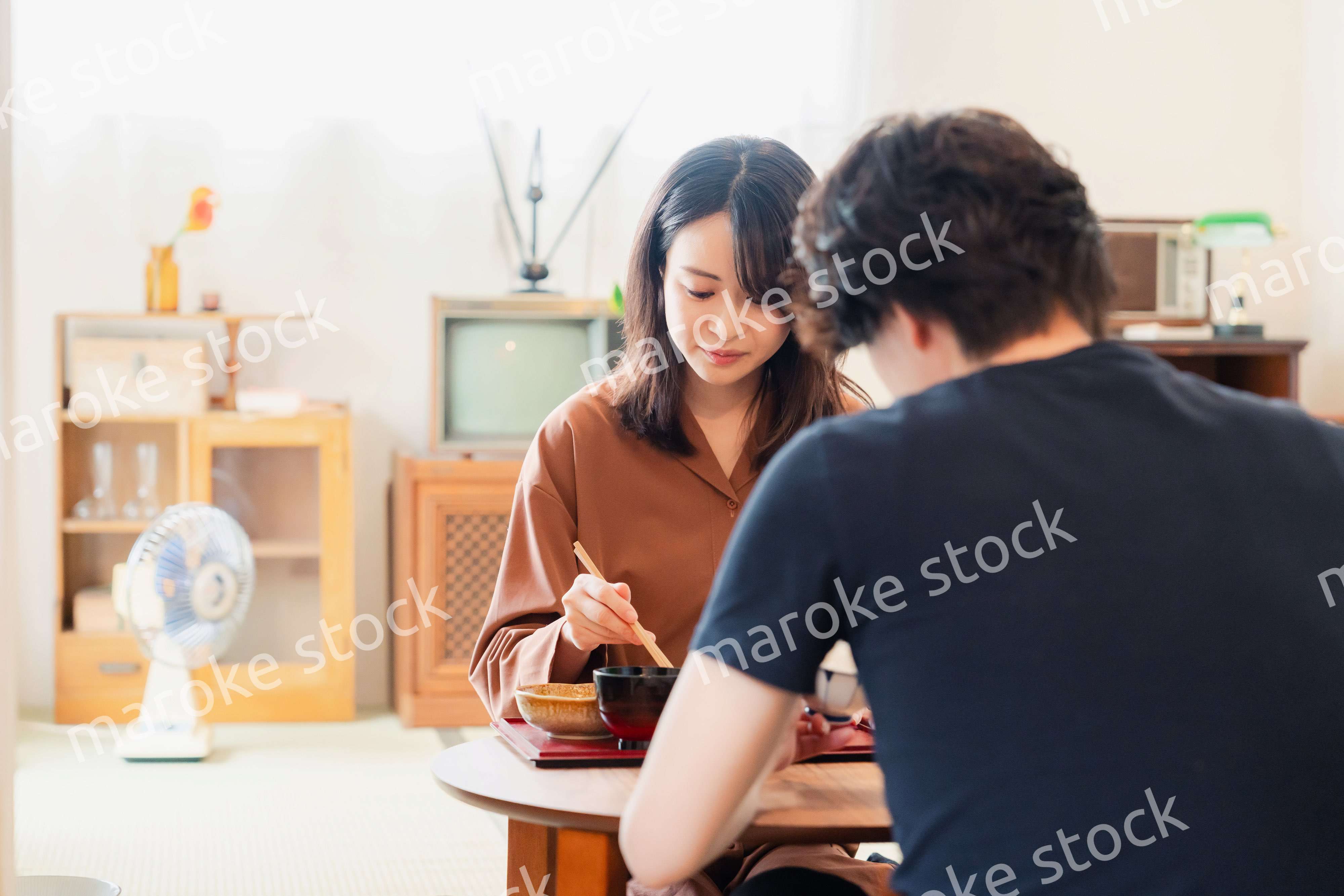 ドラマのようなレトロな雰囲気の食卓でごはんを食べる若い夫婦