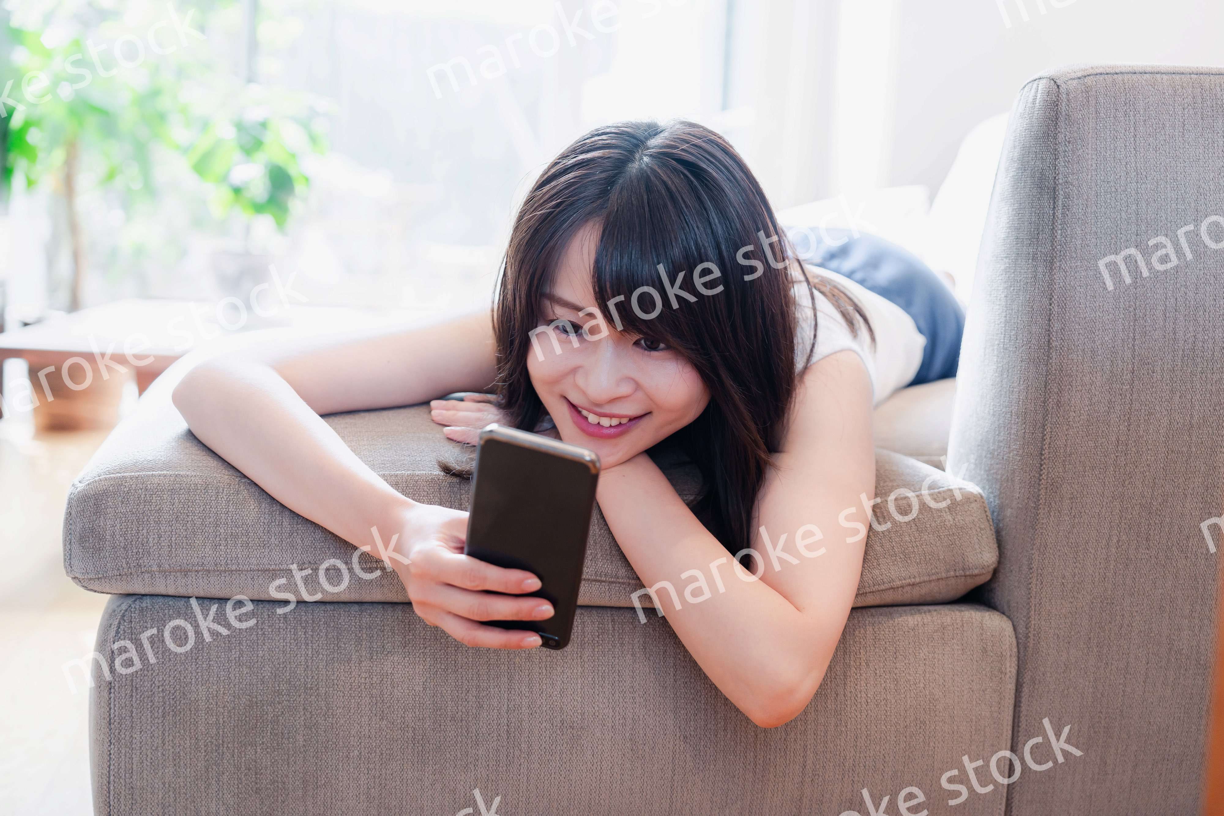 ソファでリラックスしてスマホを使う若い女性