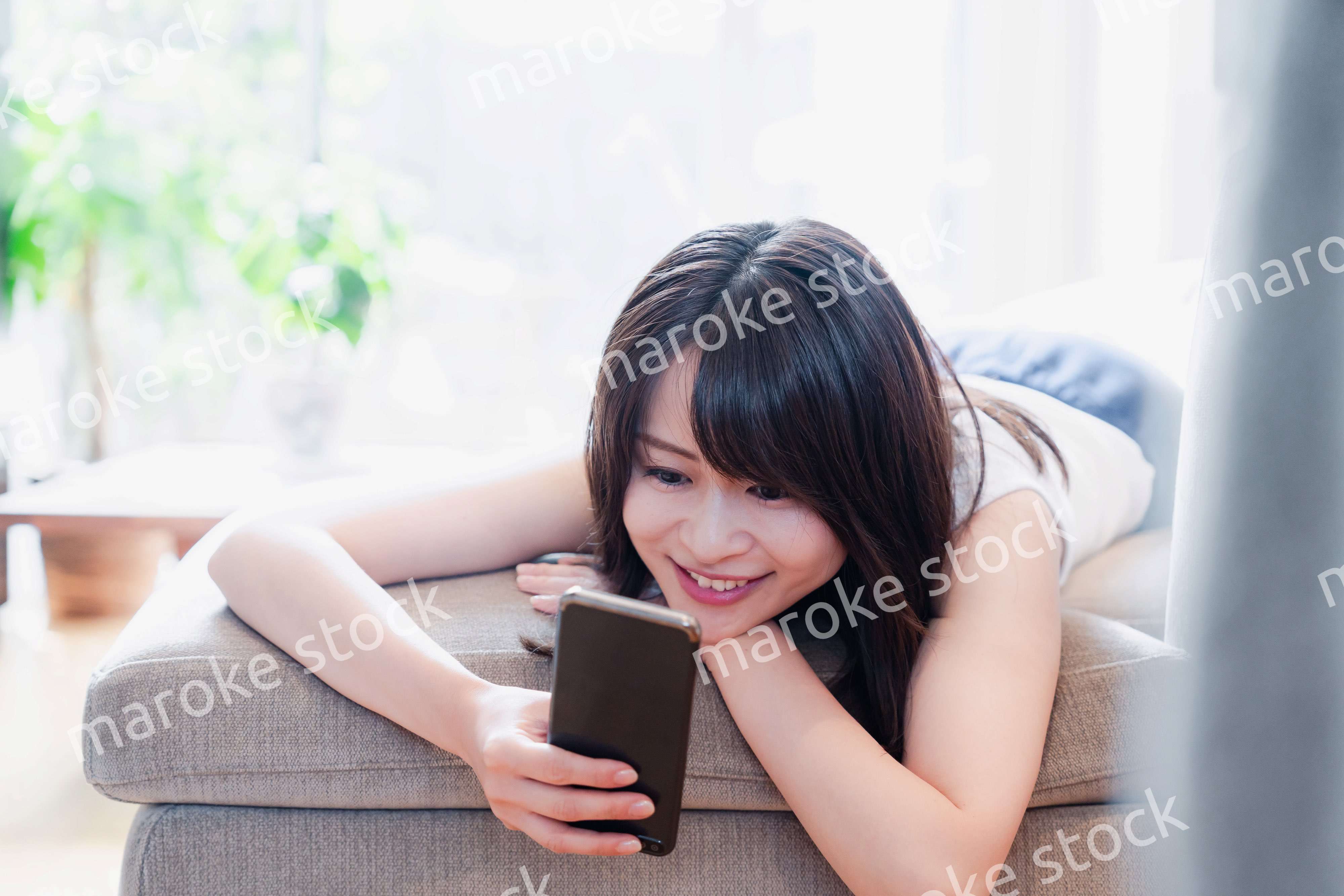 ソファでリラックスしてスマホを使う若い女性