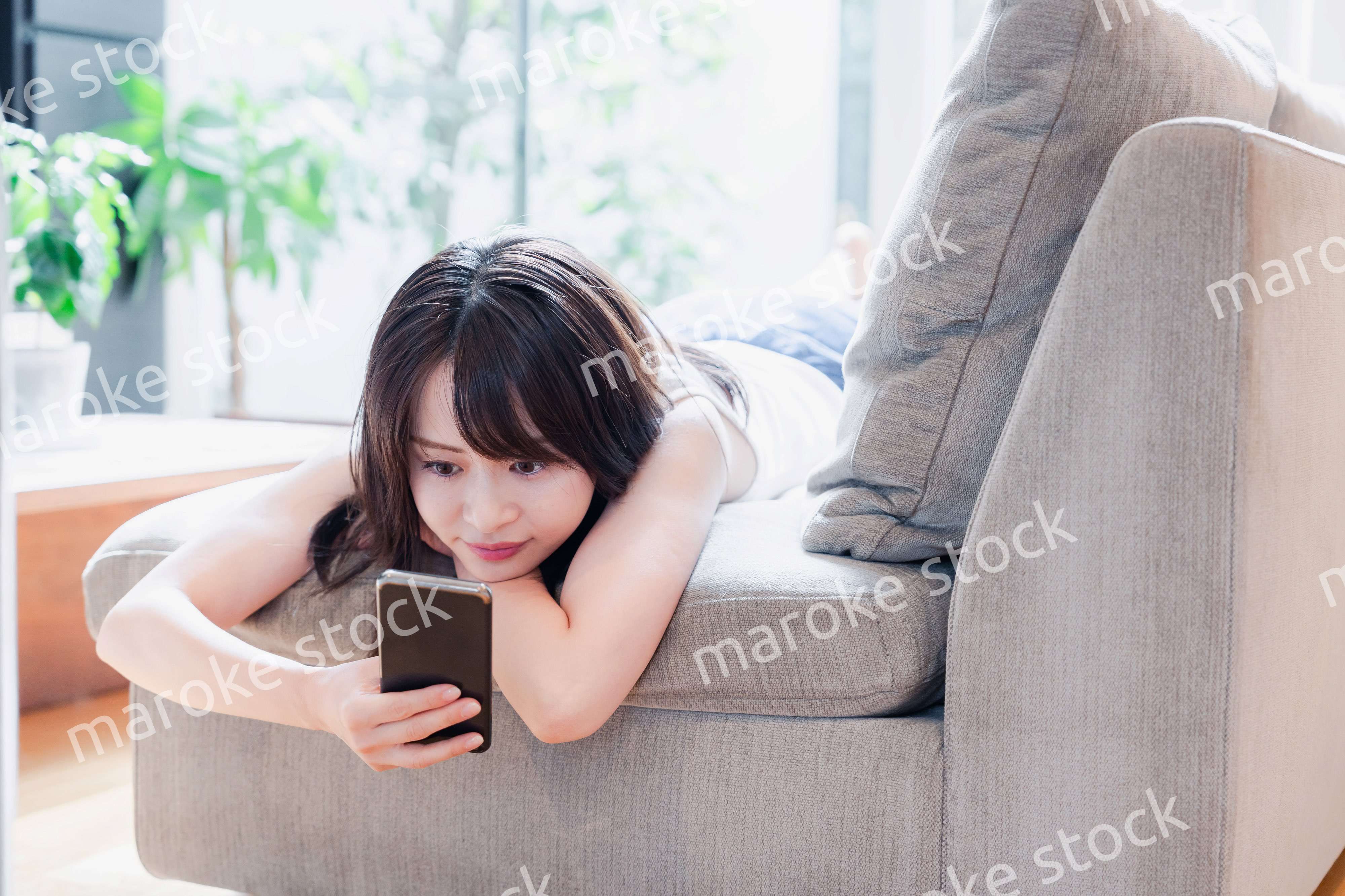 ソファでリラックスしてスマホを使う若い女性