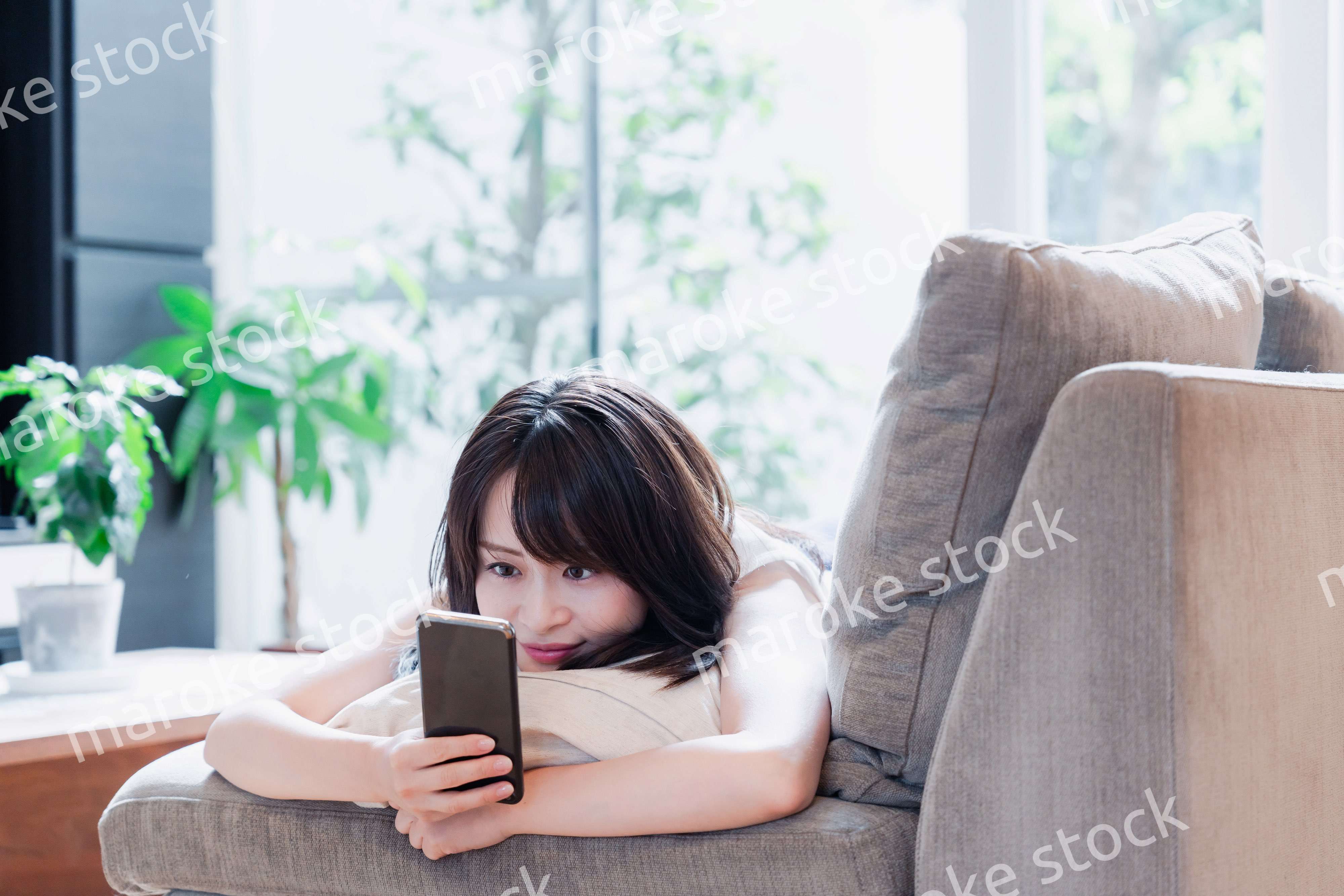 ソファでリラックスしてスマホを使う若い女性