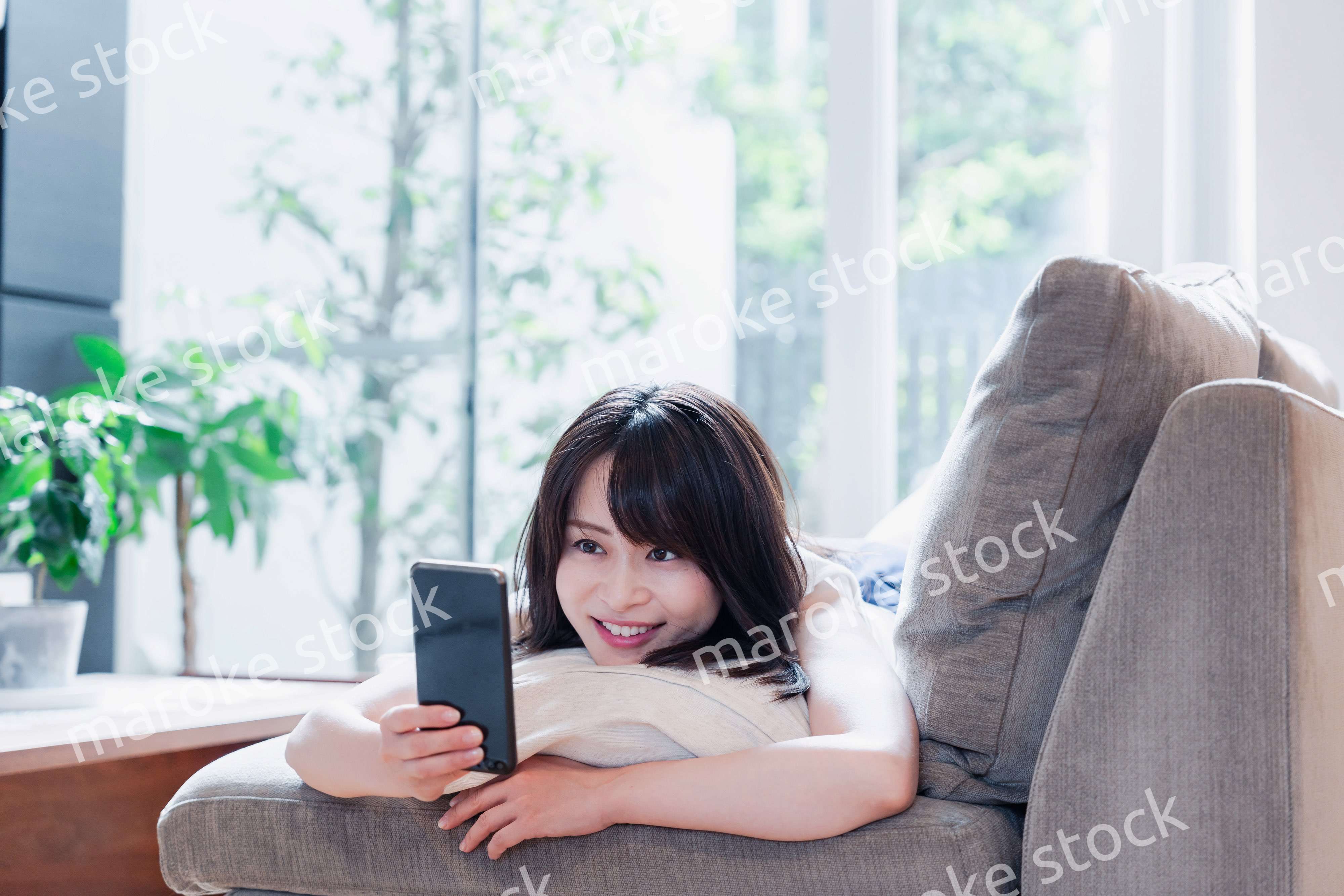 ソファでリラックスしてスマホを使う若い女性