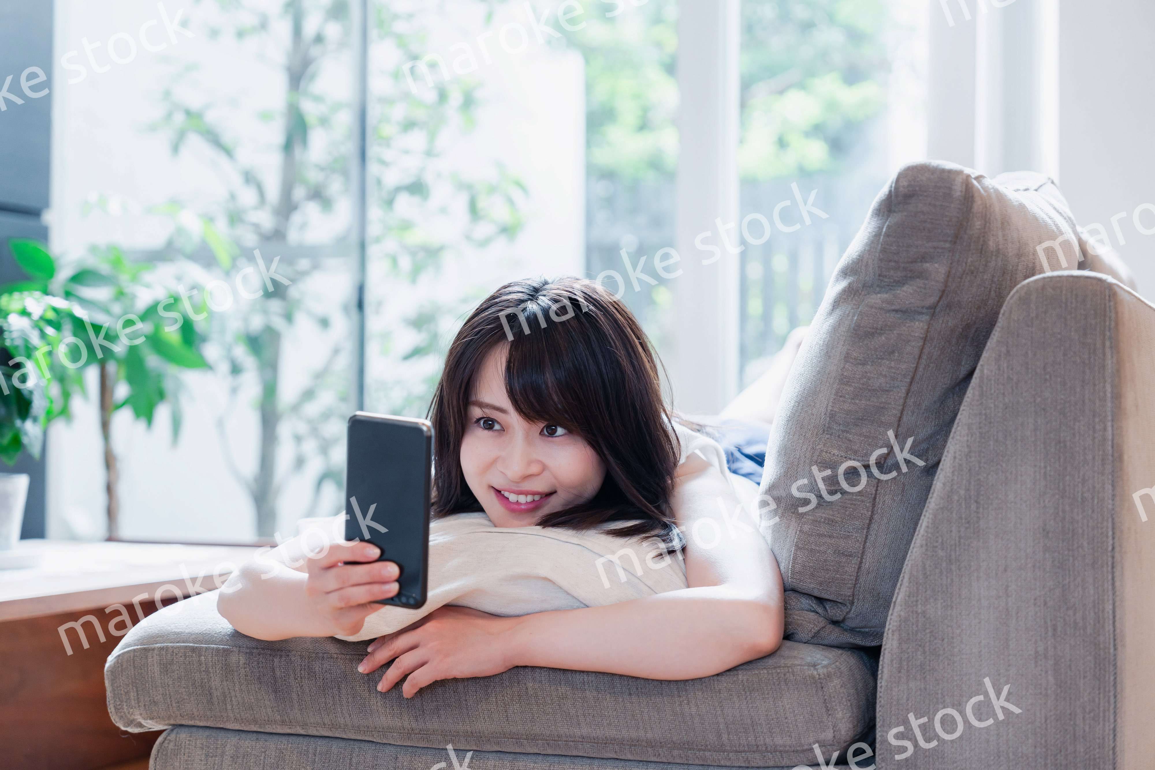 ソファでリラックスしてスマホを使う若い女性