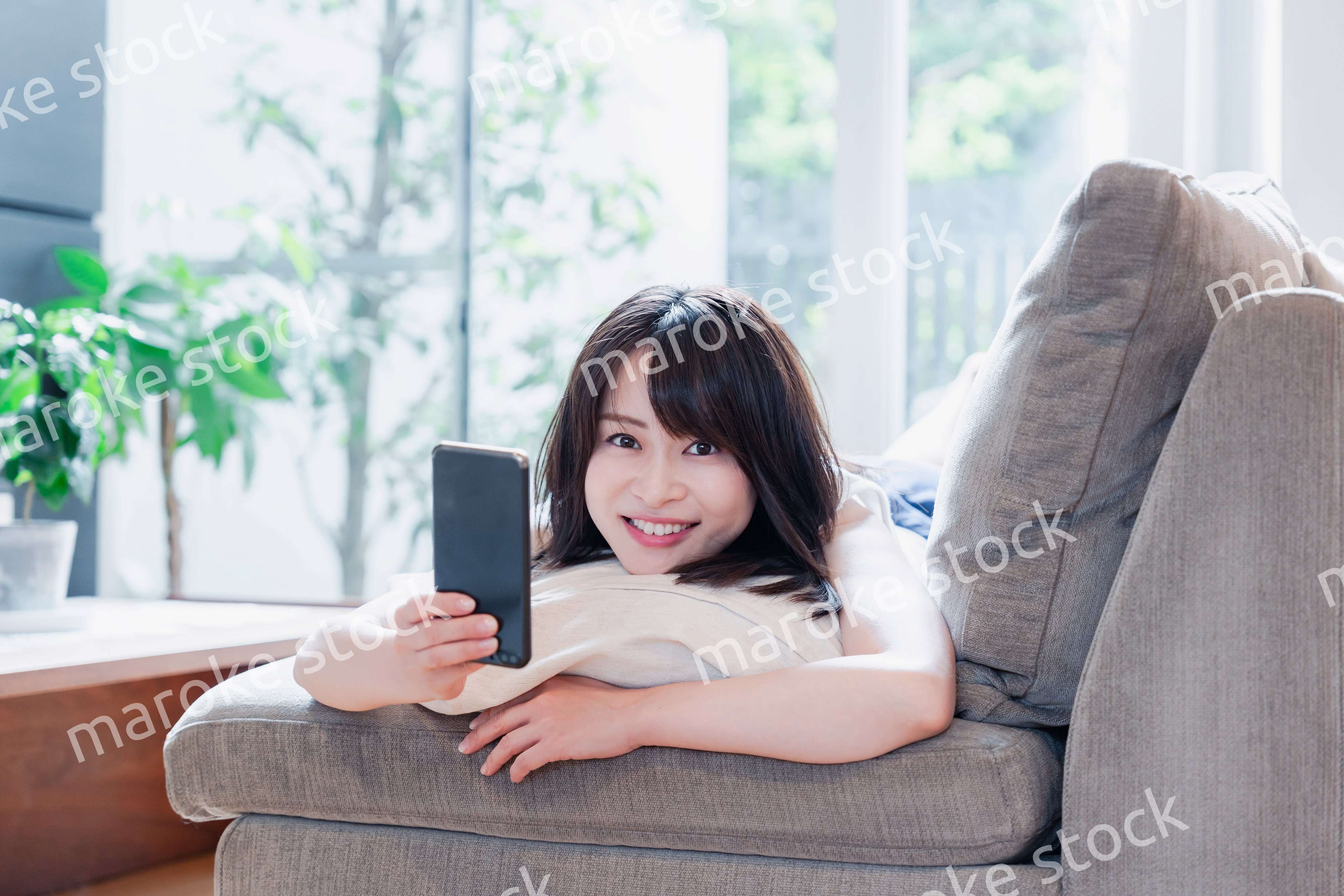 ソファでリラックスしてスマホを使う若い女性