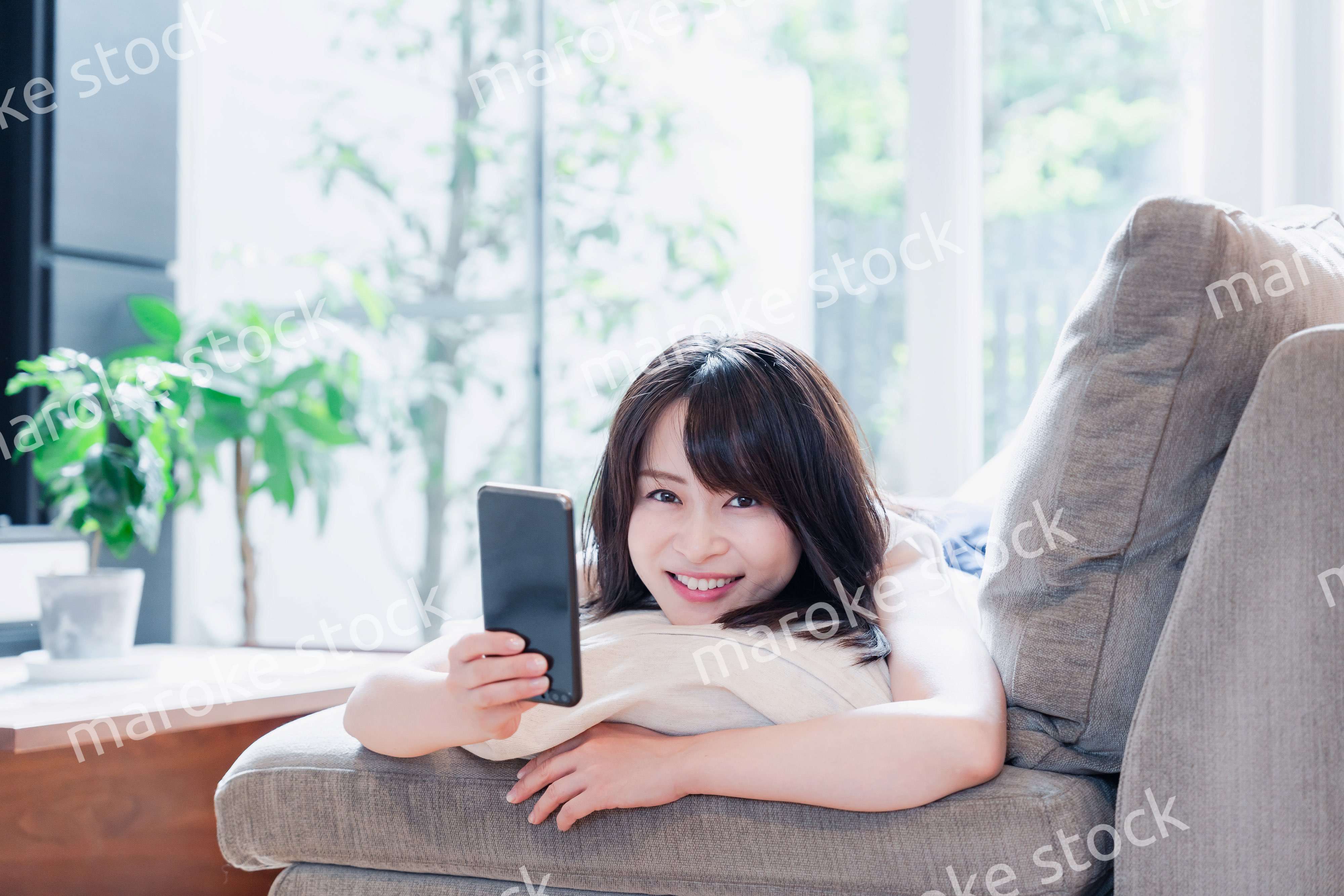 ソファでリラックスしてスマホを使う若い女性