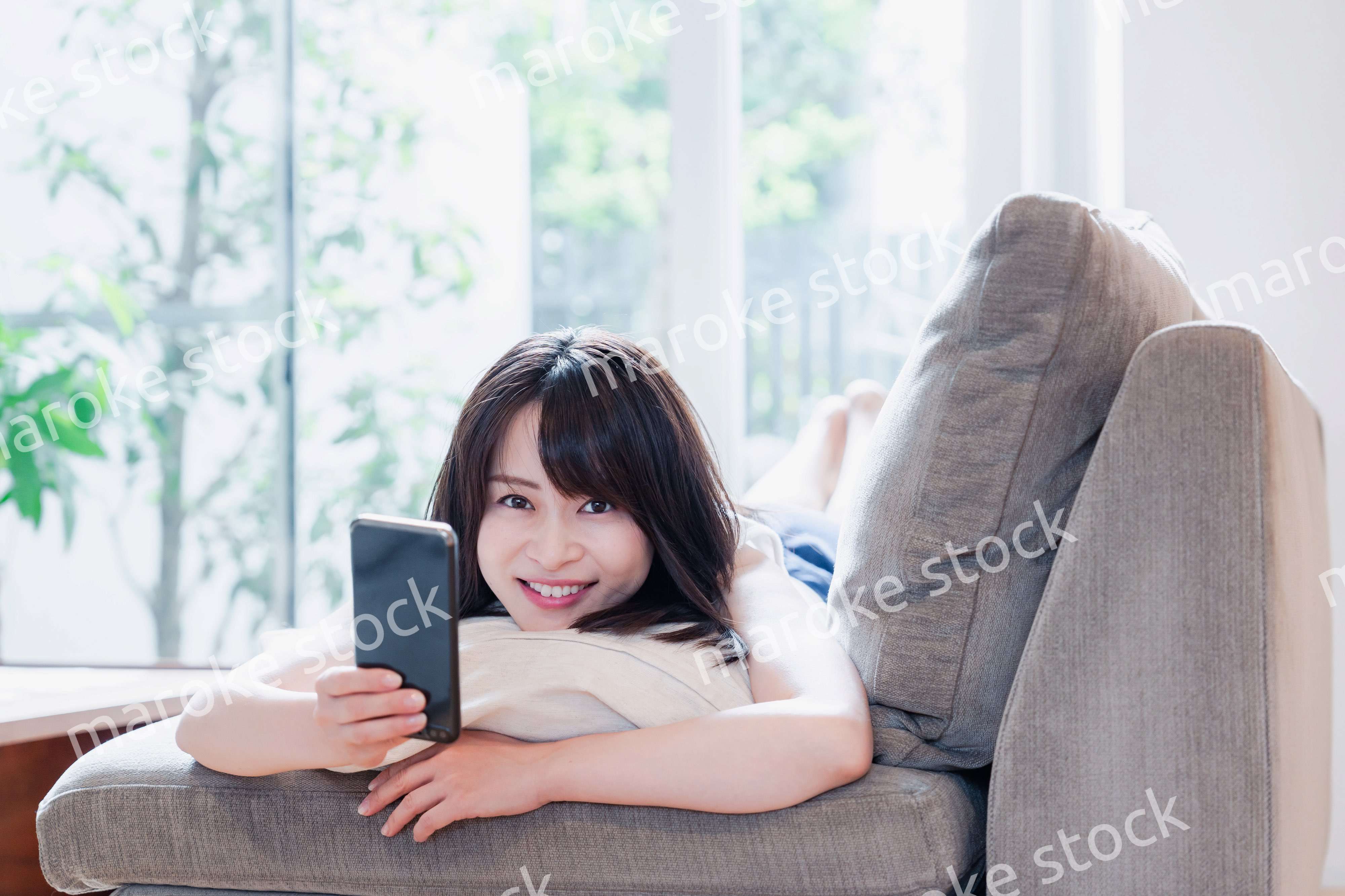 ソファでリラックスしてスマホを使う若い女性