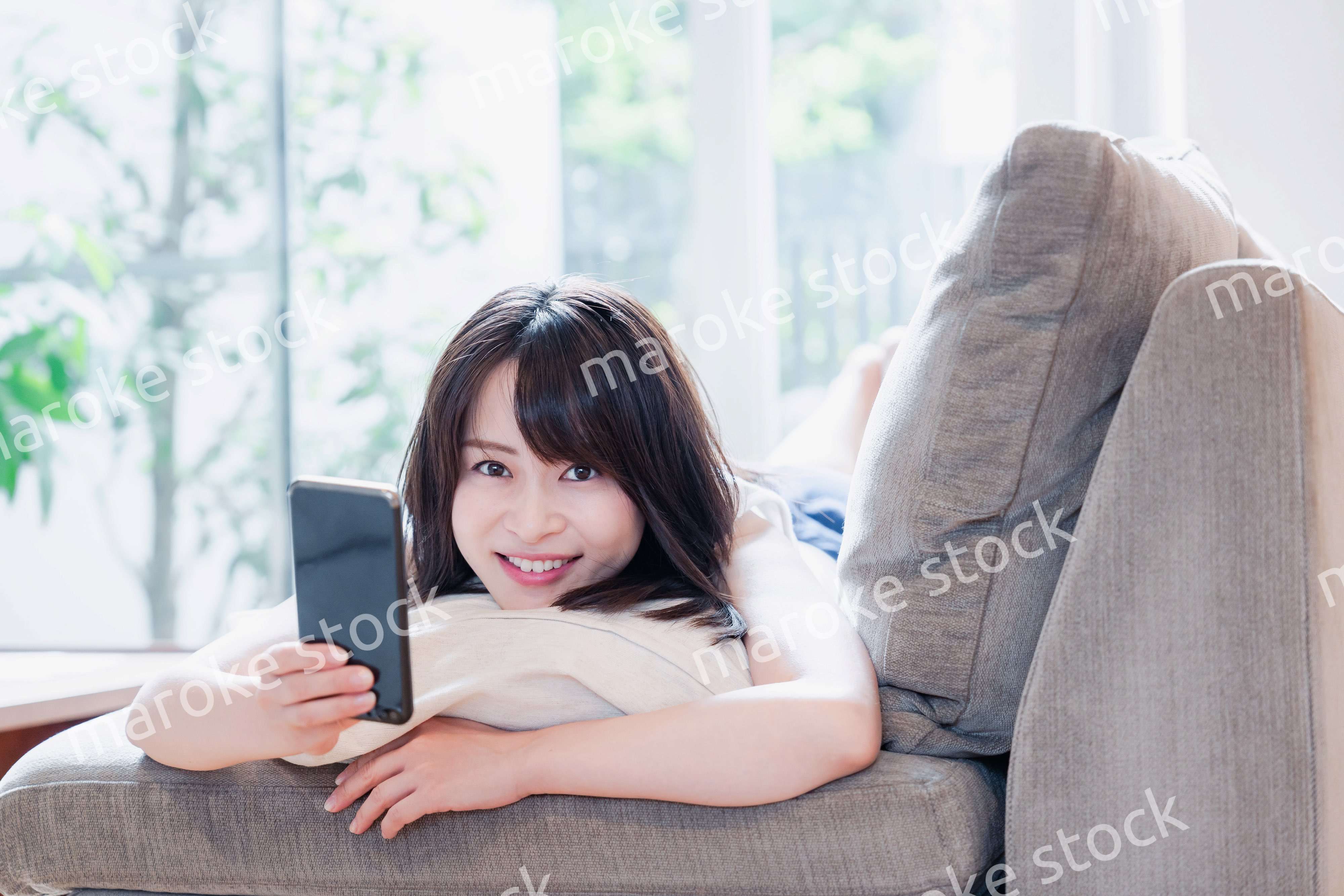 ソファでリラックスしてスマホを使う若い女性