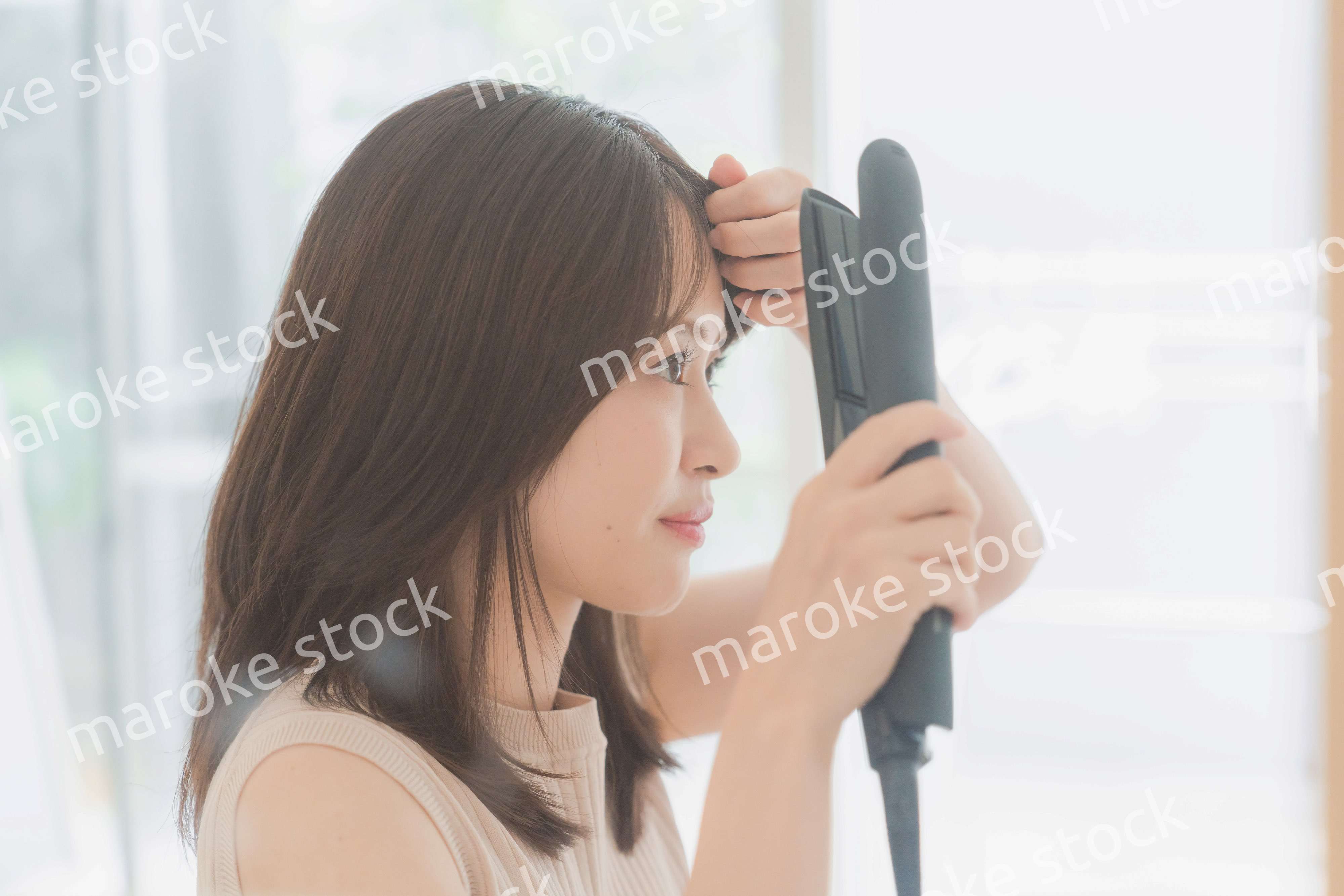 ヘアアイロンを使って髪をセットする若い女性