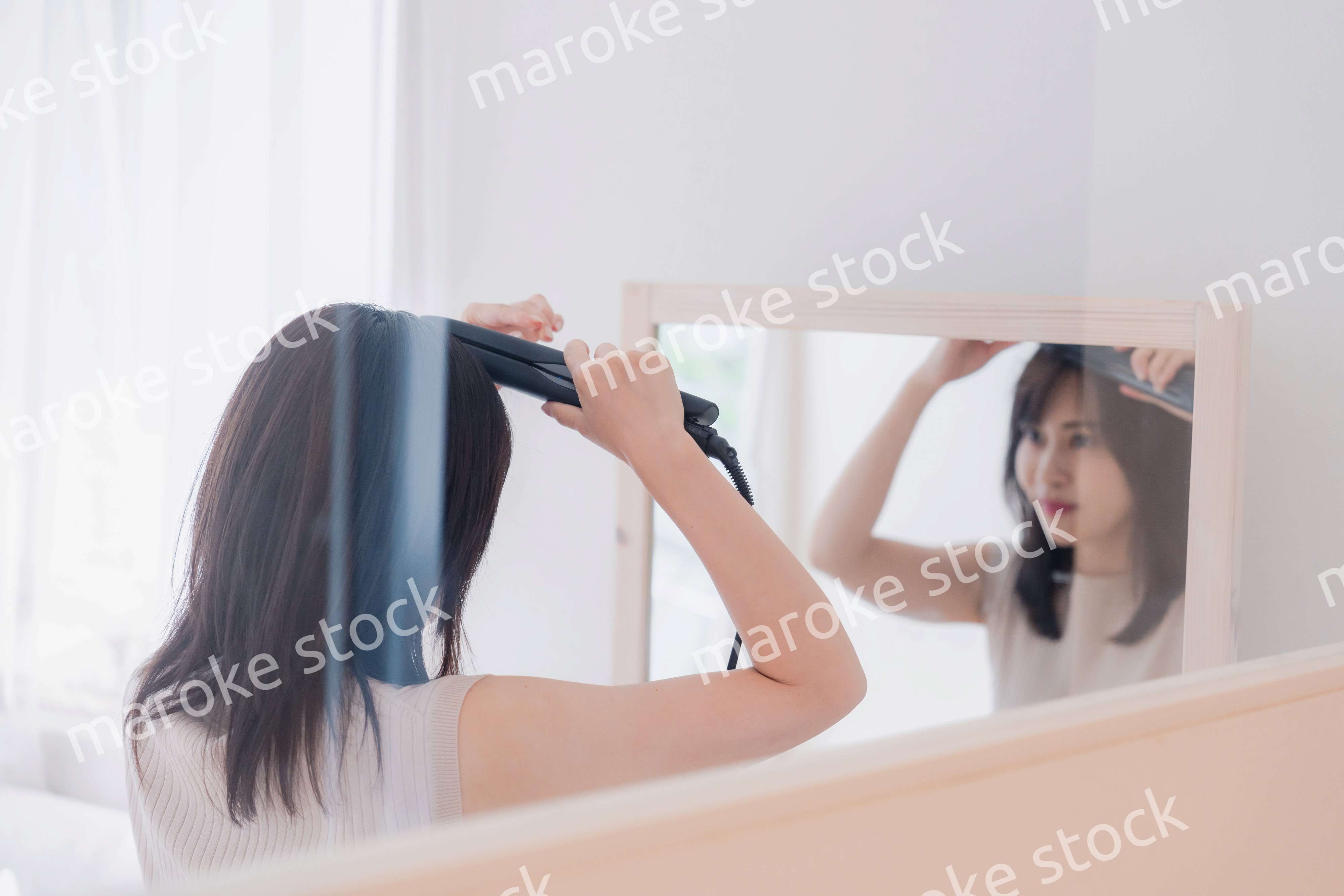 ヘアアイロンを使って髪をセットする若い女性