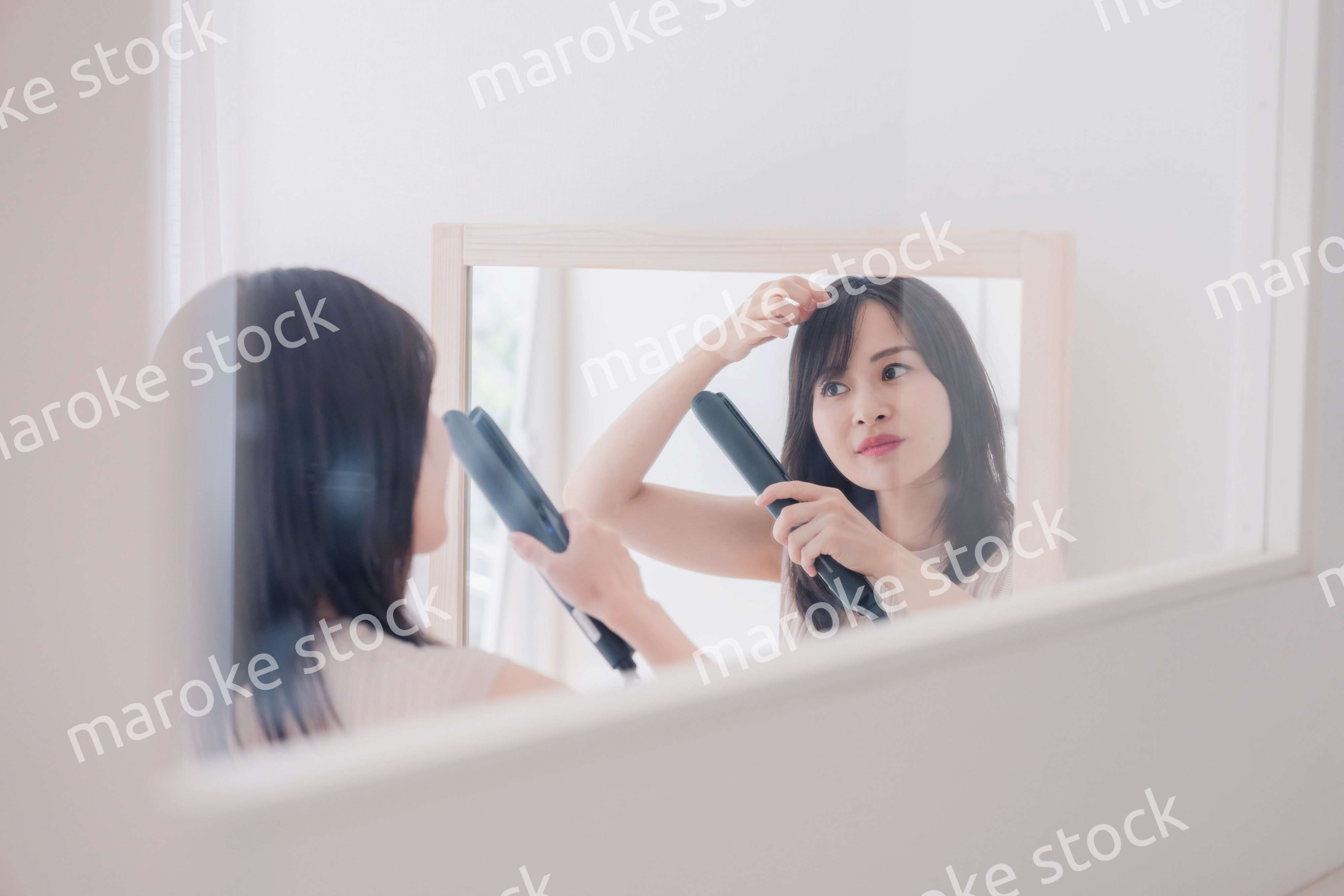 ヘアアイロンを使って髪をセットする若い女性