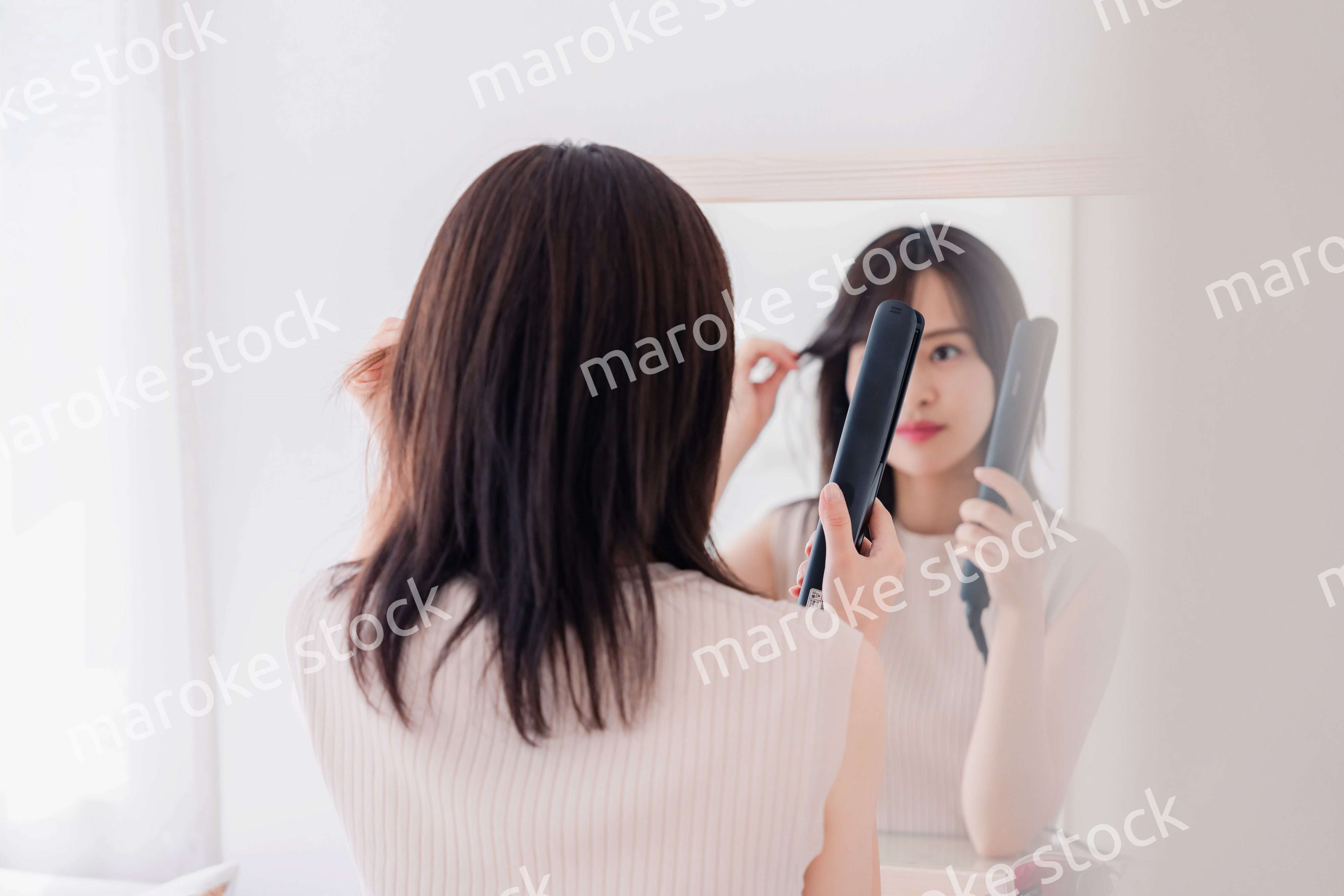 ヘアアイロンを使って髪をセットする若い女性