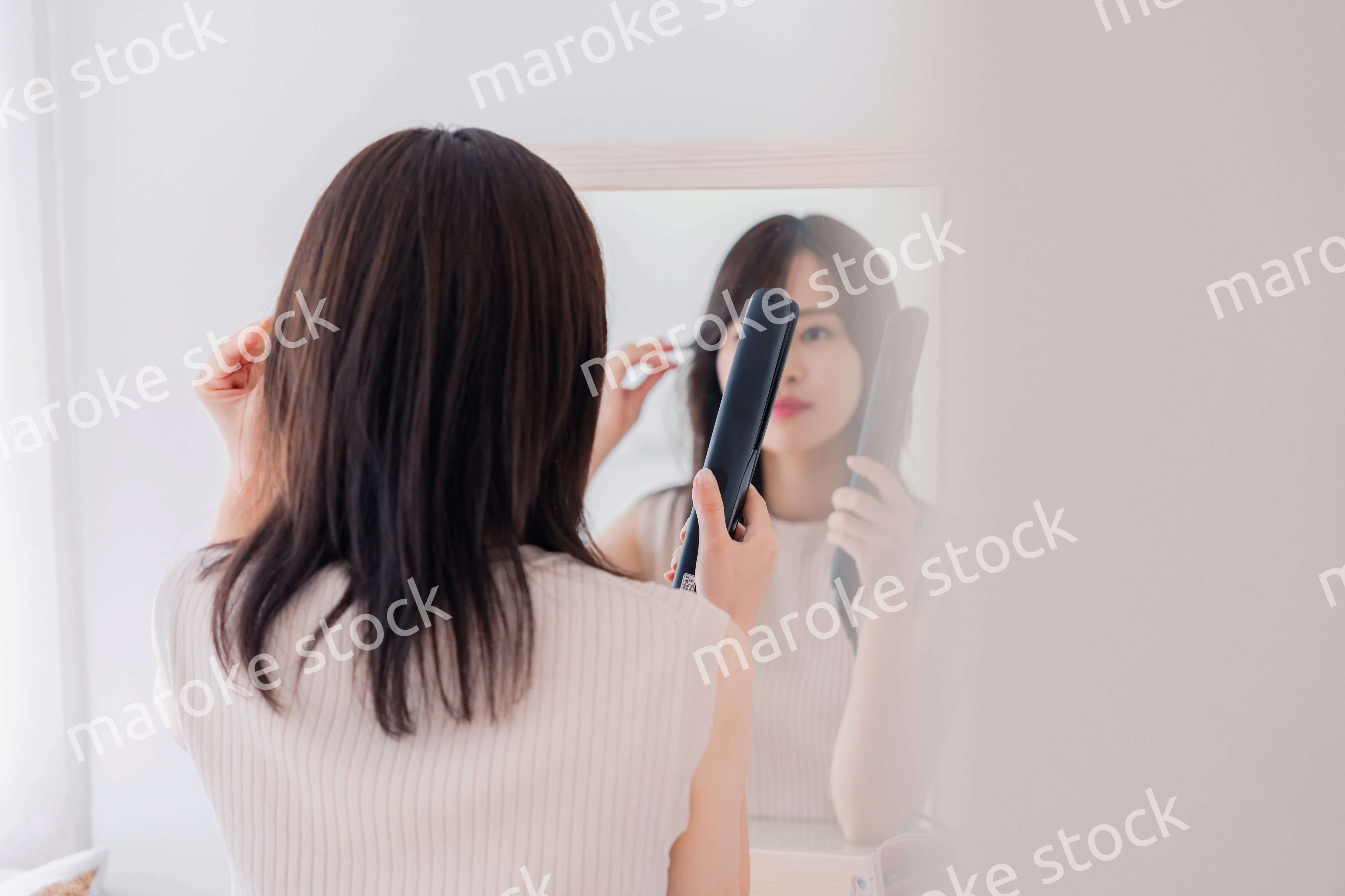 ヘアアイロンを使って髪をセットする若い女性