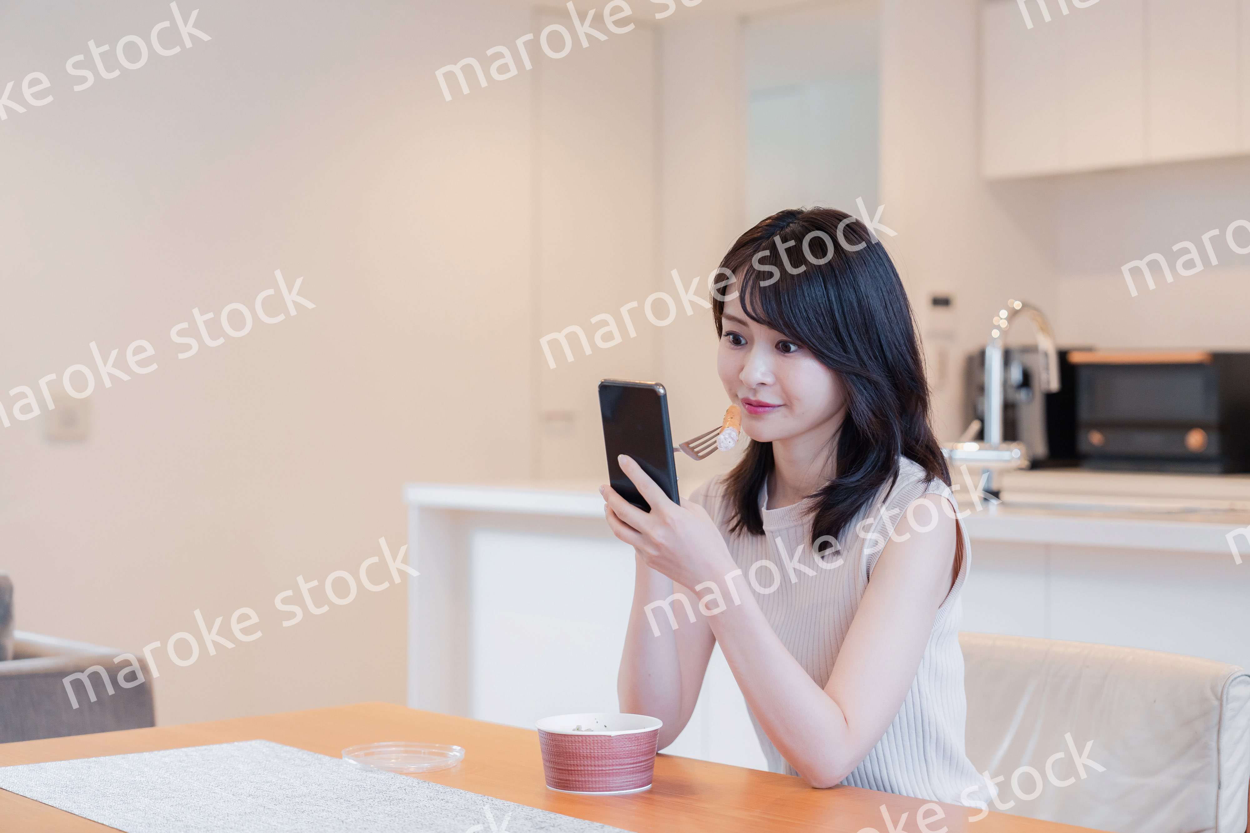 家でスマホを使いながらごはんを食べる若い女性