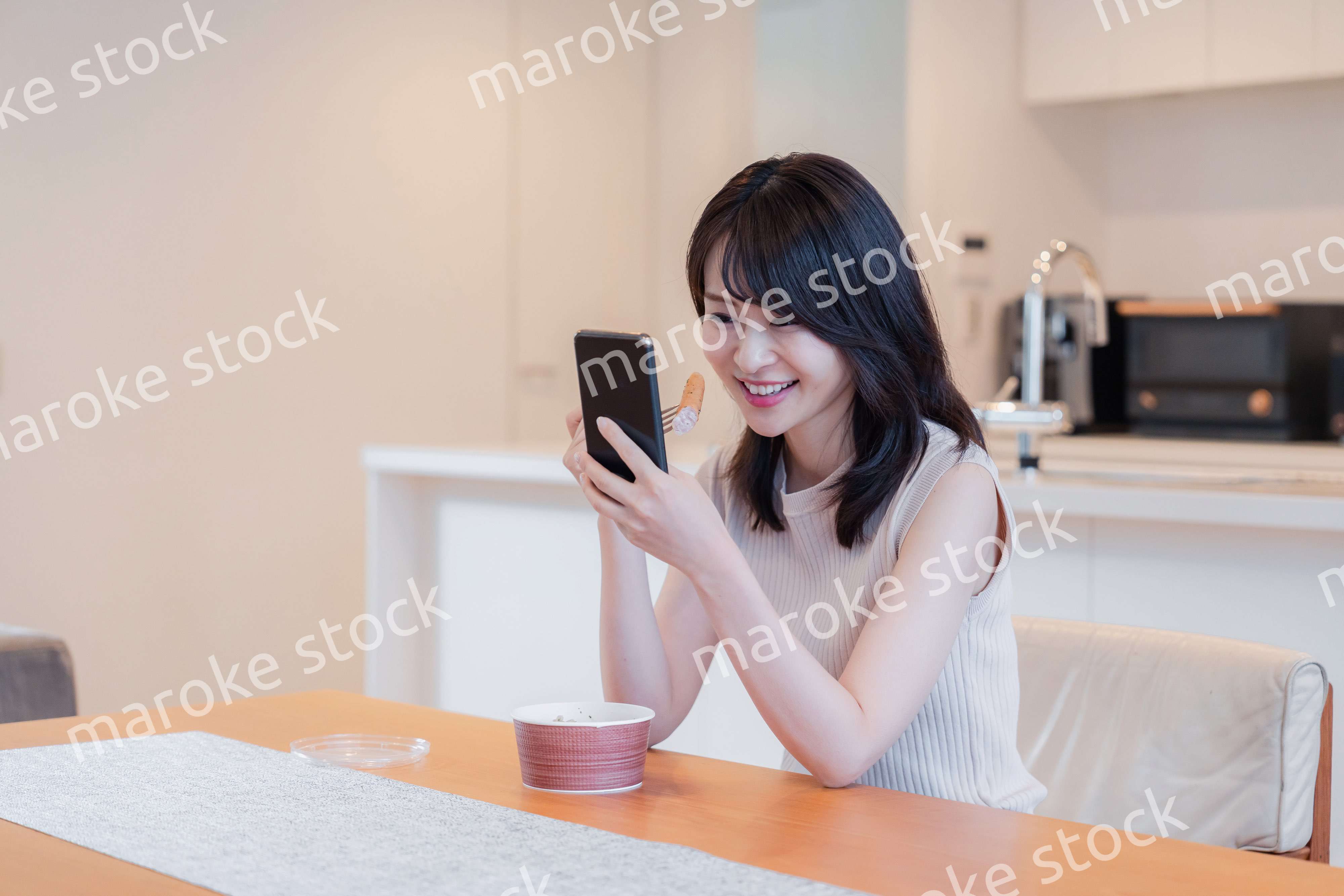 家でスマホを使いながらごはんを食べる若い女性