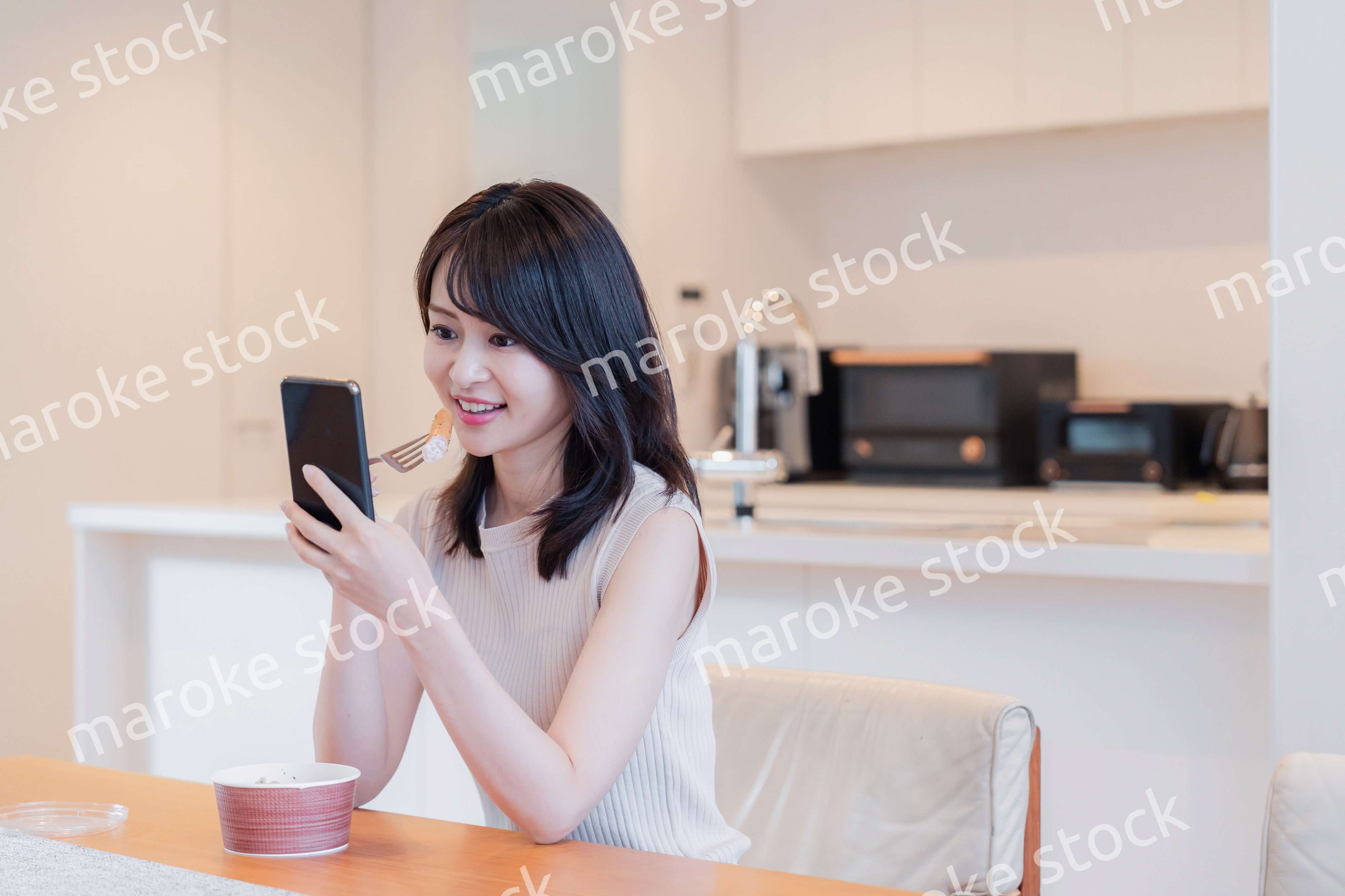 家でスマホを使いながらごはんを食べる若い女性