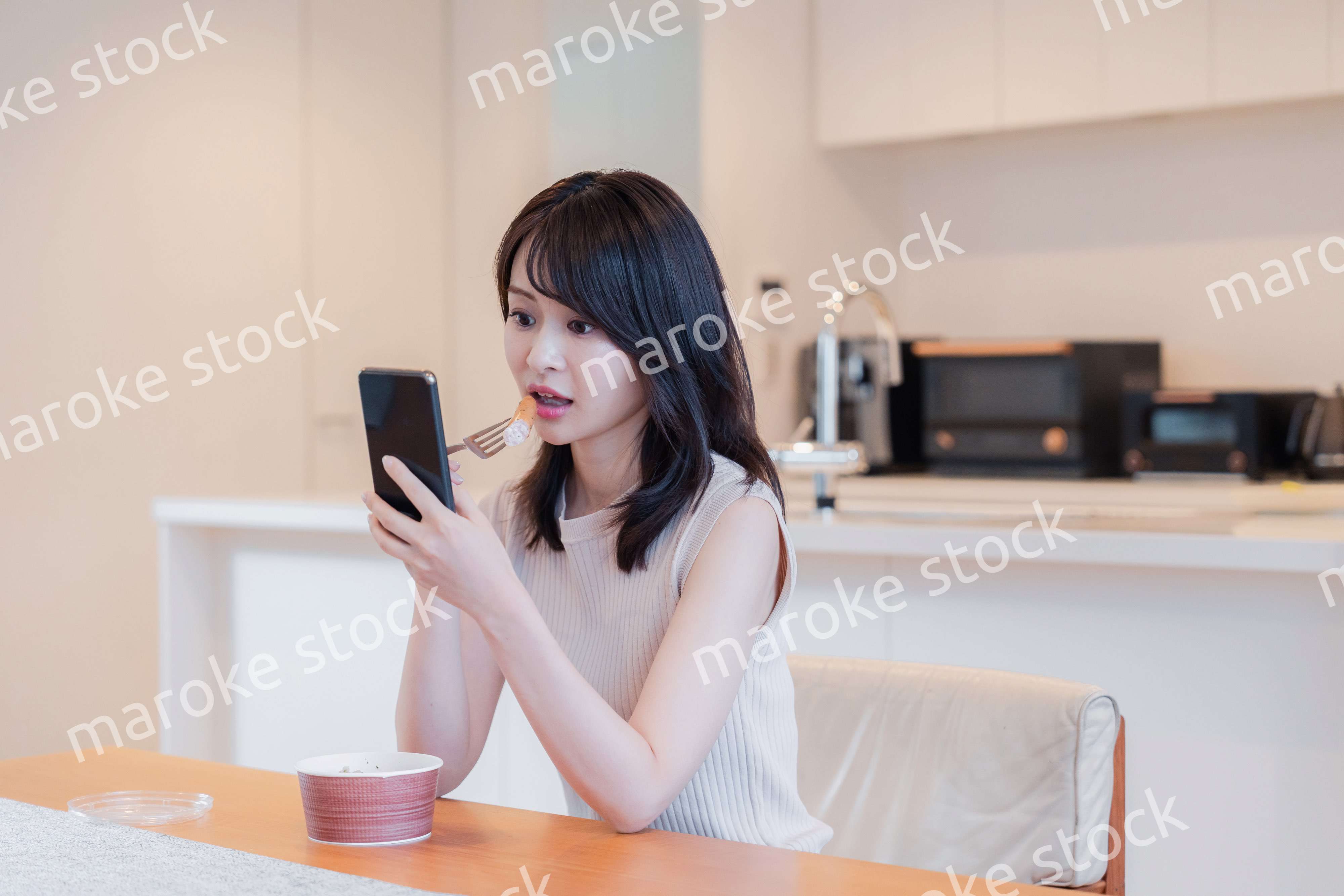 家でスマホを使いながらごはんを食べる若い女性