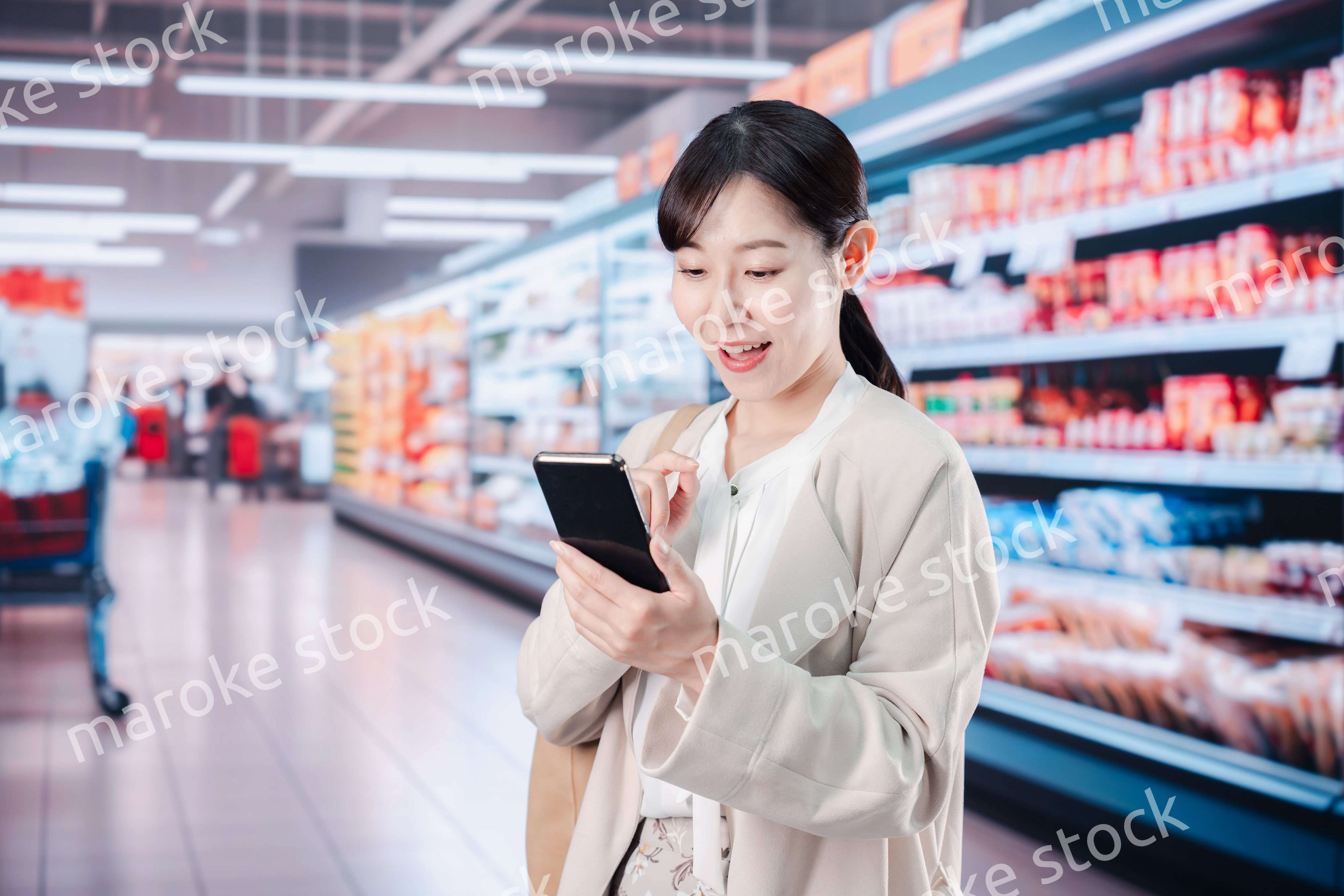 スマホを使いながらスーパーで買い物をする主婦