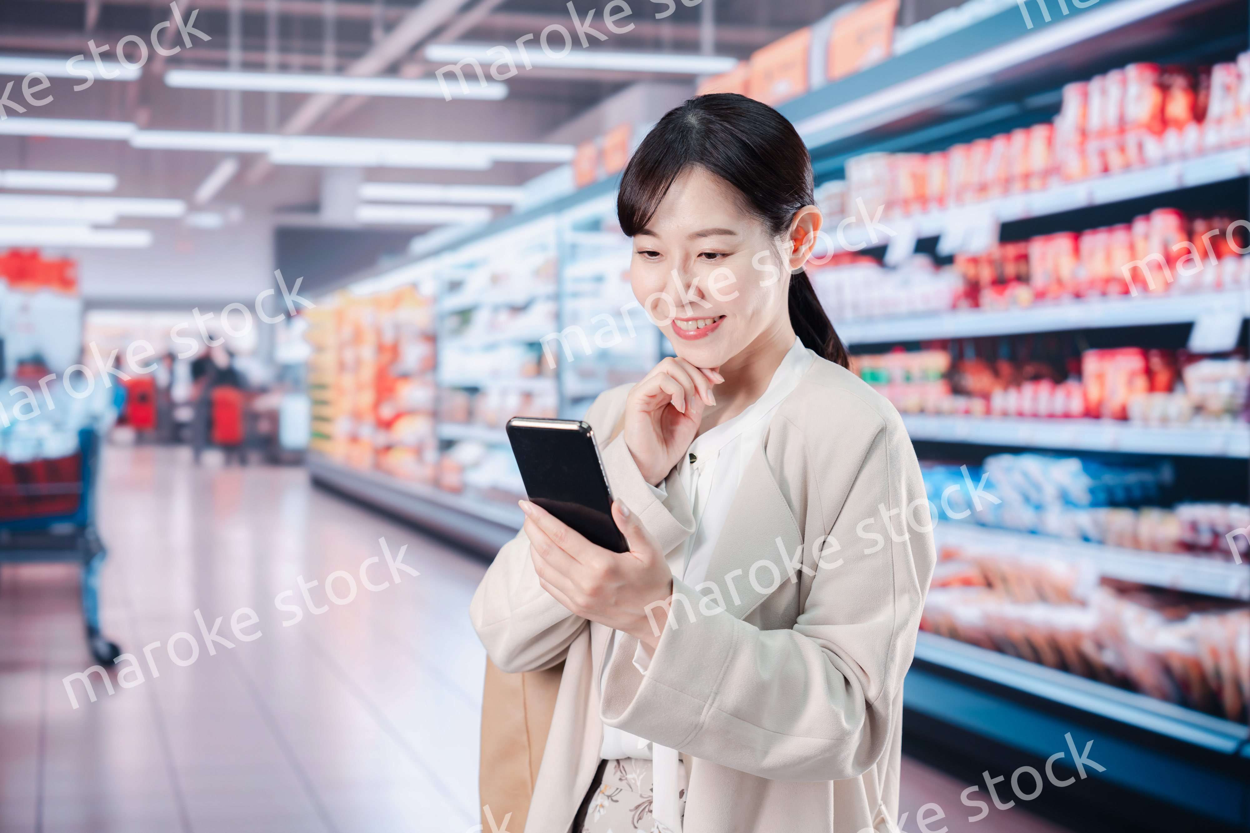 スマホを使いながらスーパーで買い物をする主婦