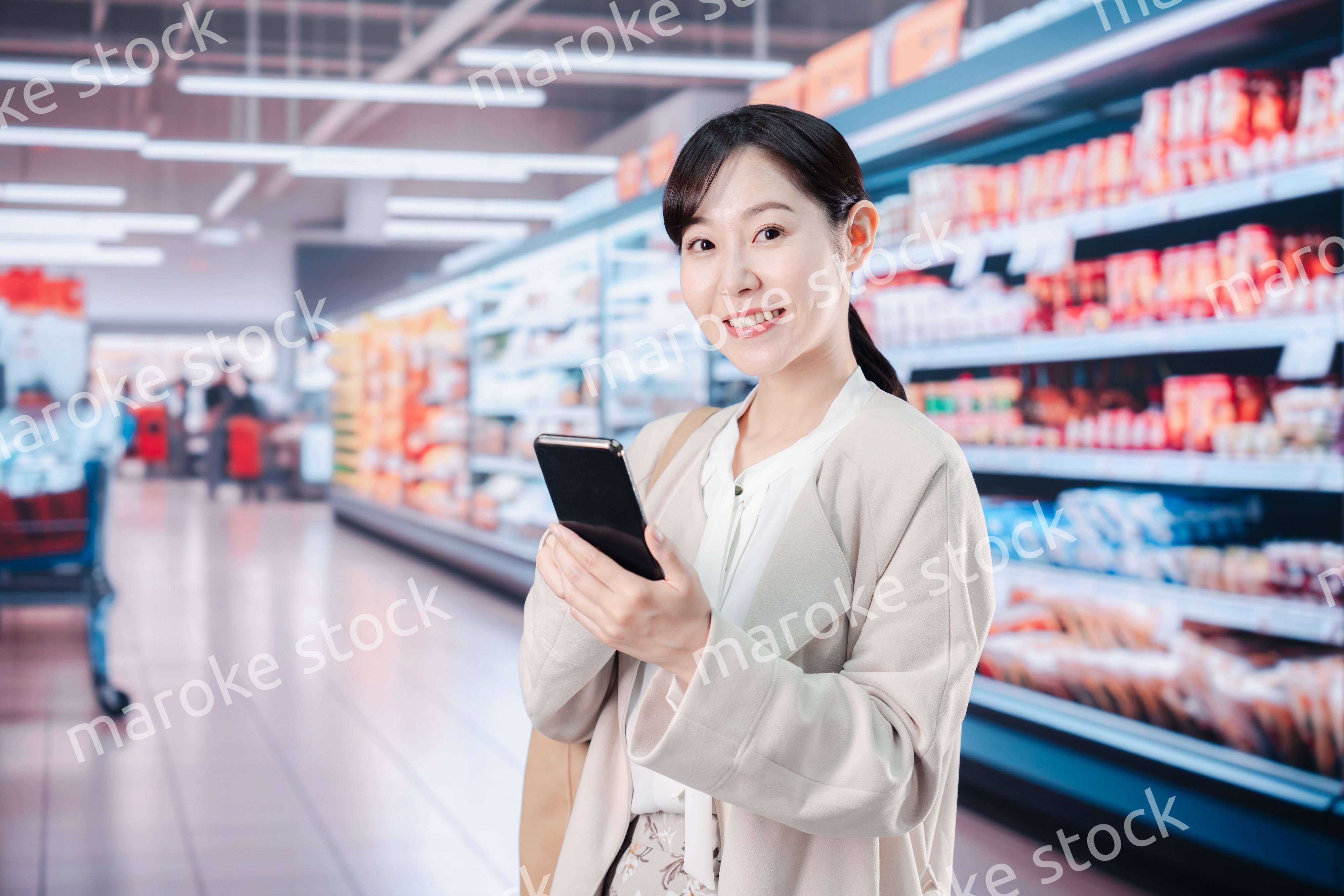 スマホを使いながらスーパーで買い物をする主婦