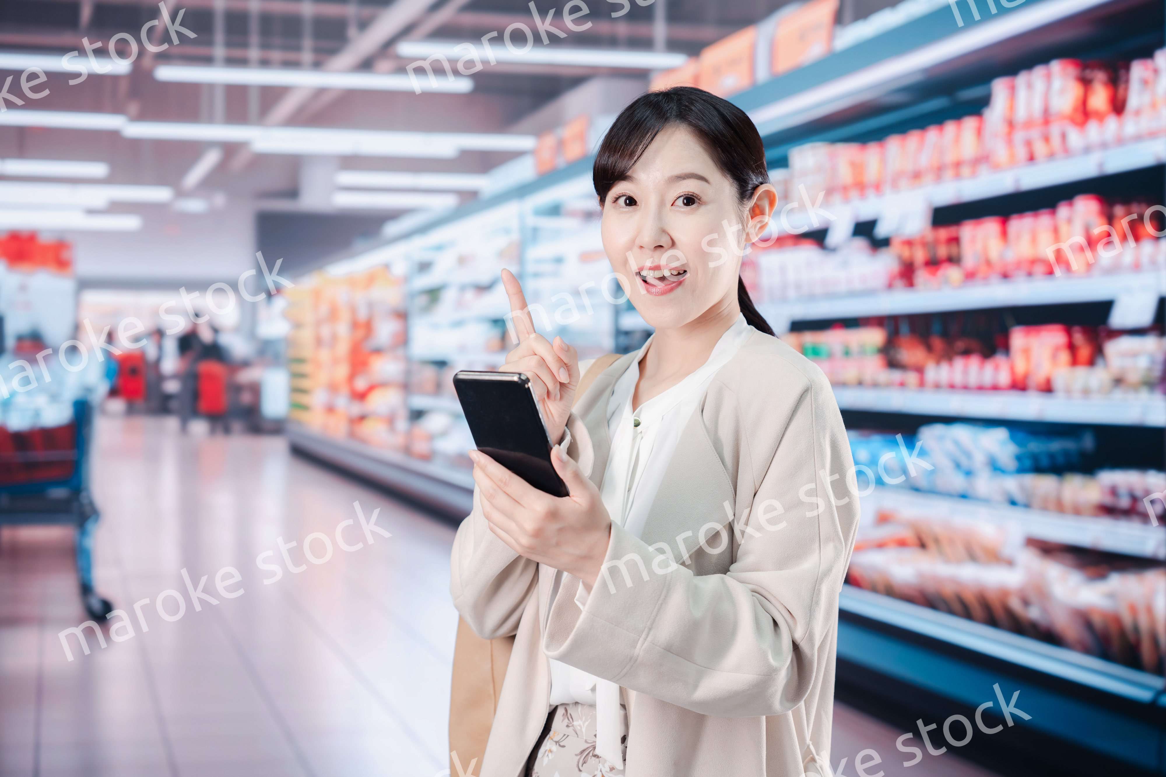 スマホを使いながらスーパーで買い物をする主婦