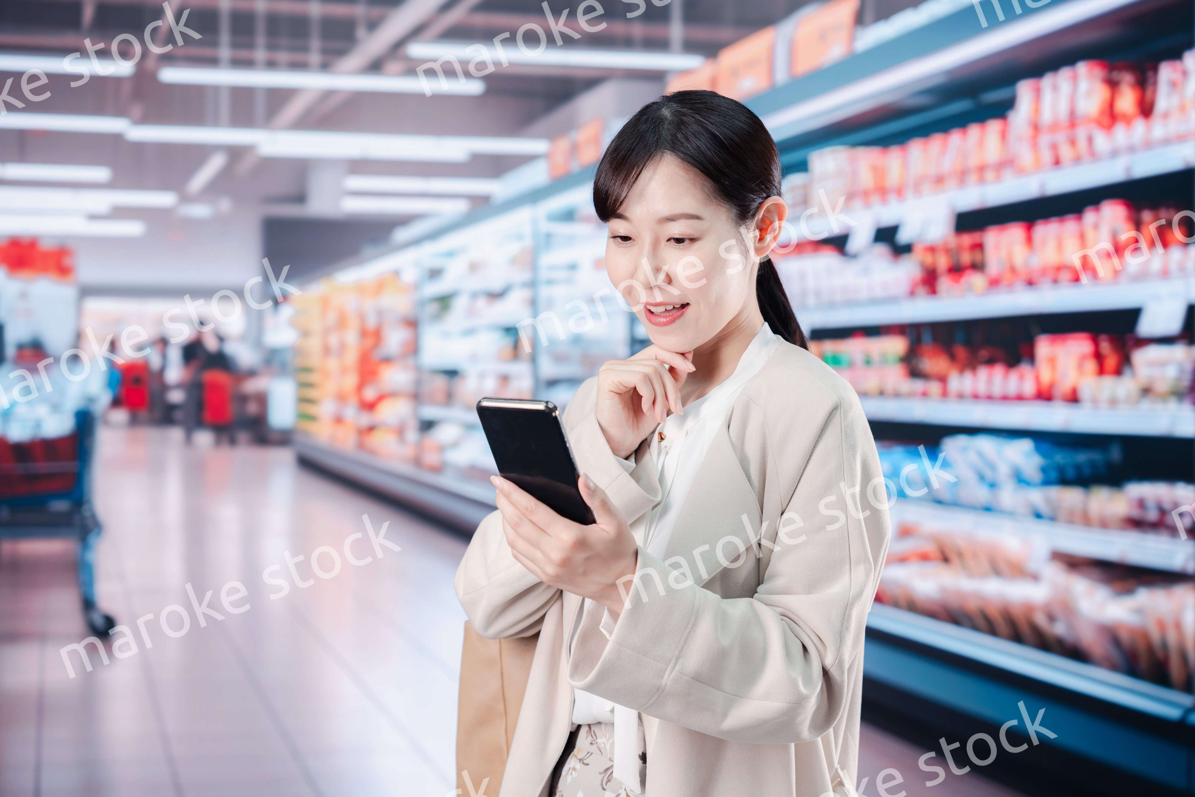 スマホを使いながらスーパーで買い物をする主婦