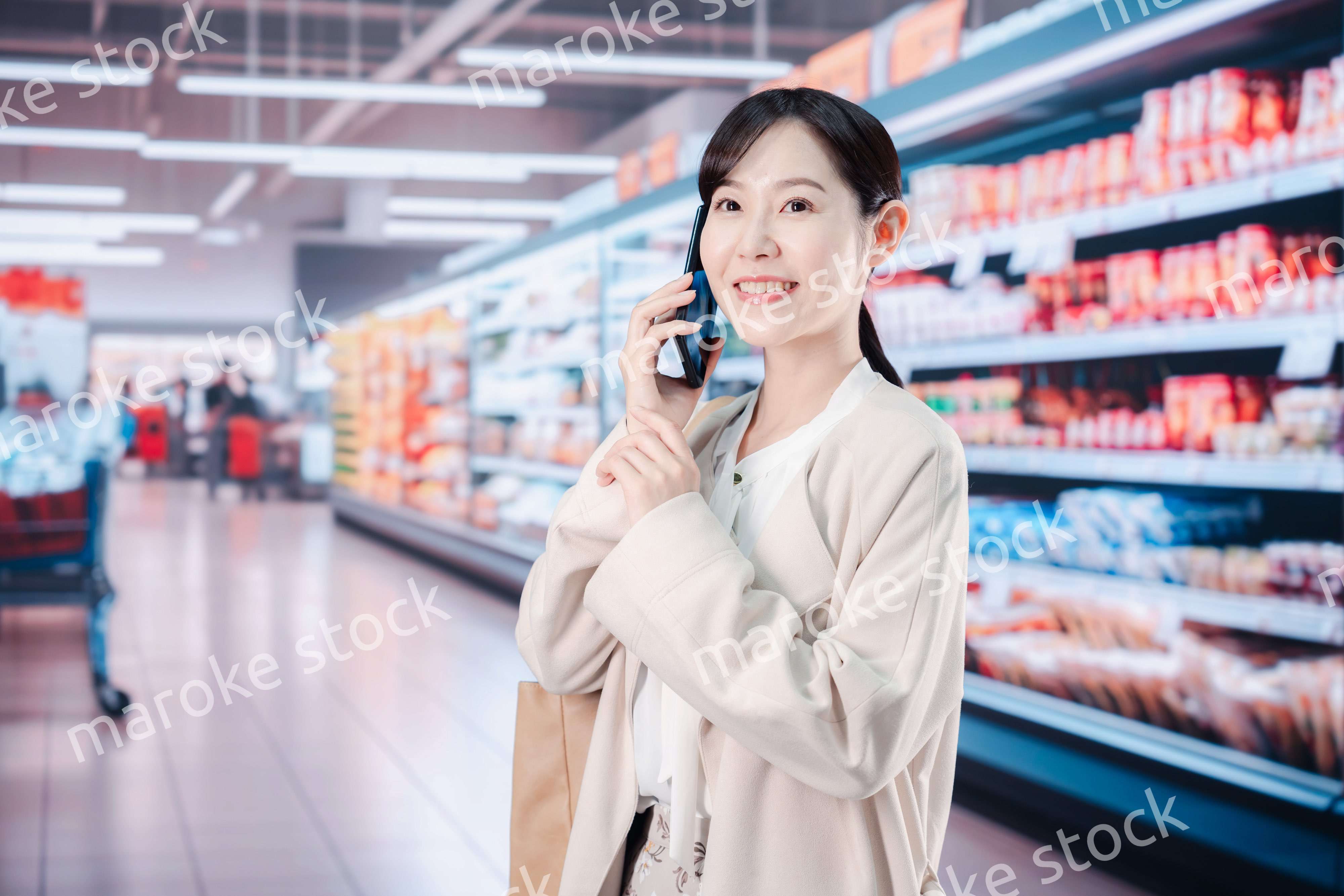 スマホを使いながらスーパーで買い物をする主婦