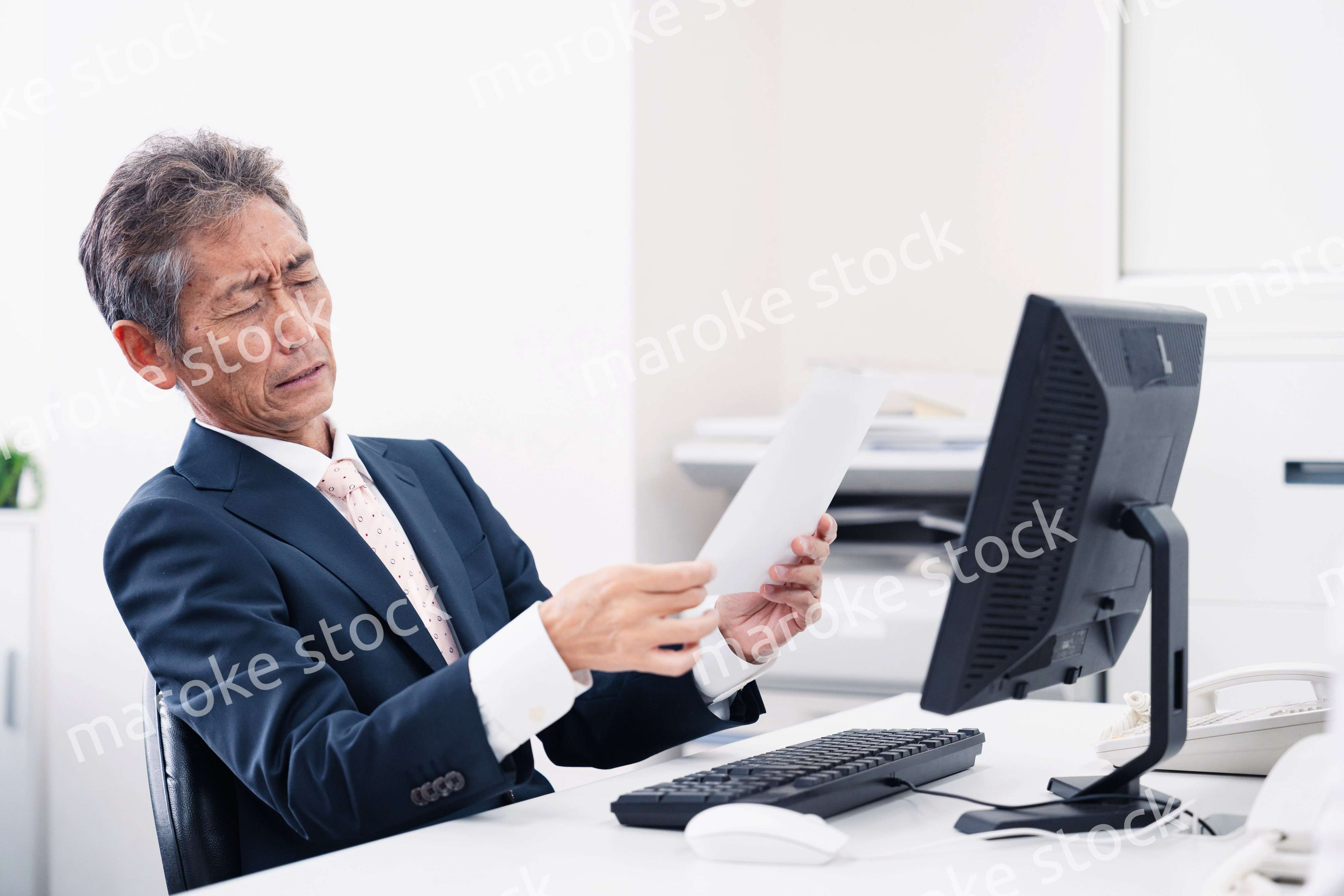 老眼で書類が見づらい高齢のビジネスマン