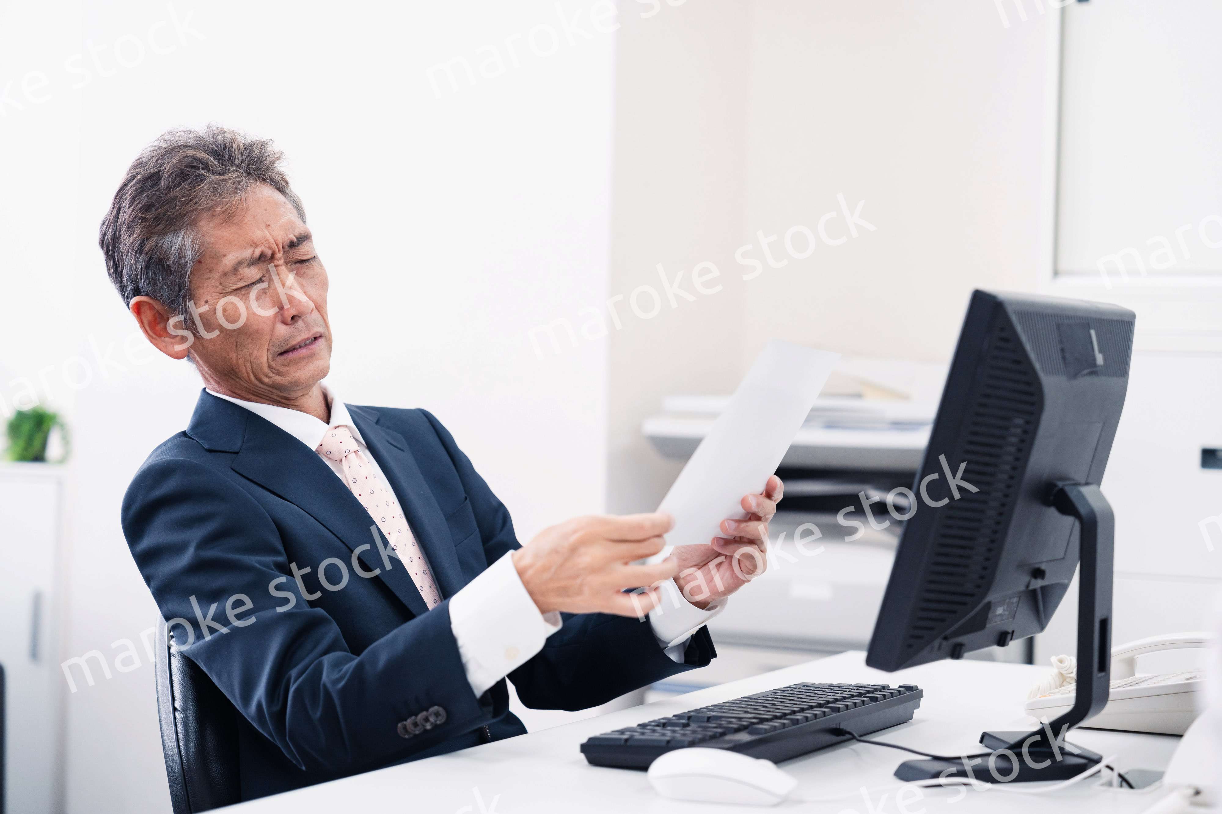 老眼で書類が見づらい高齢のビジネスマン