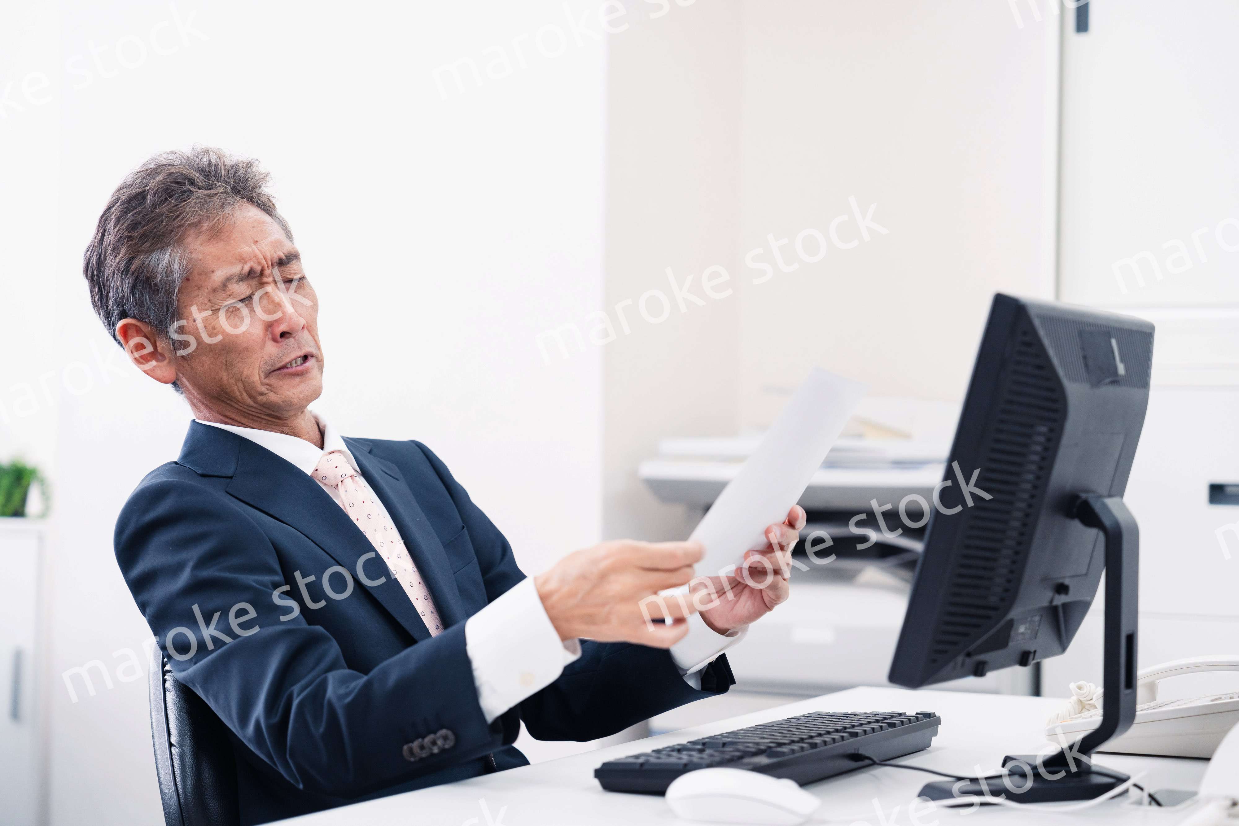 老眼で書類が見づらい高齢のビジネスマン