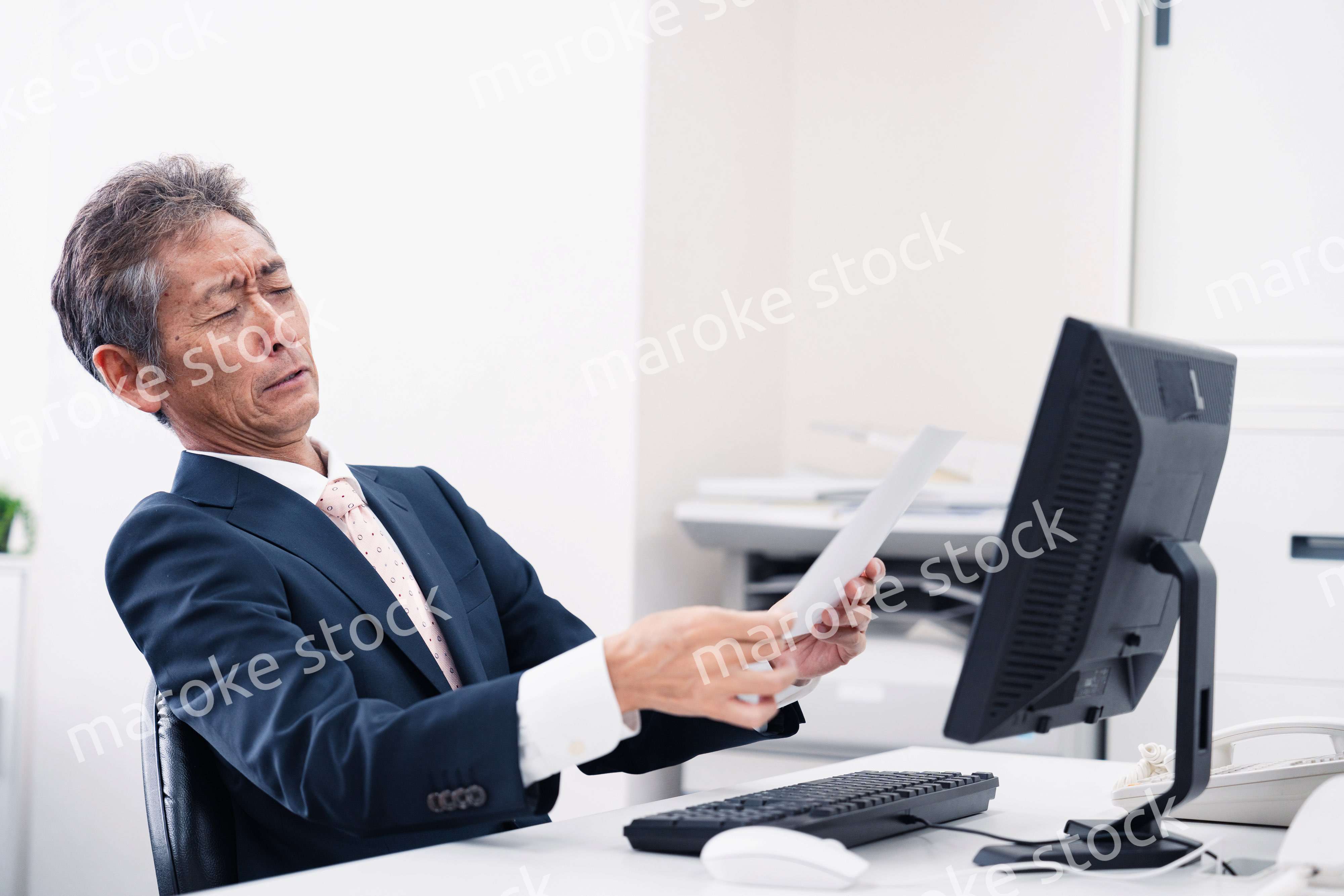 老眼で書類が見づらい高齢のビジネスマン