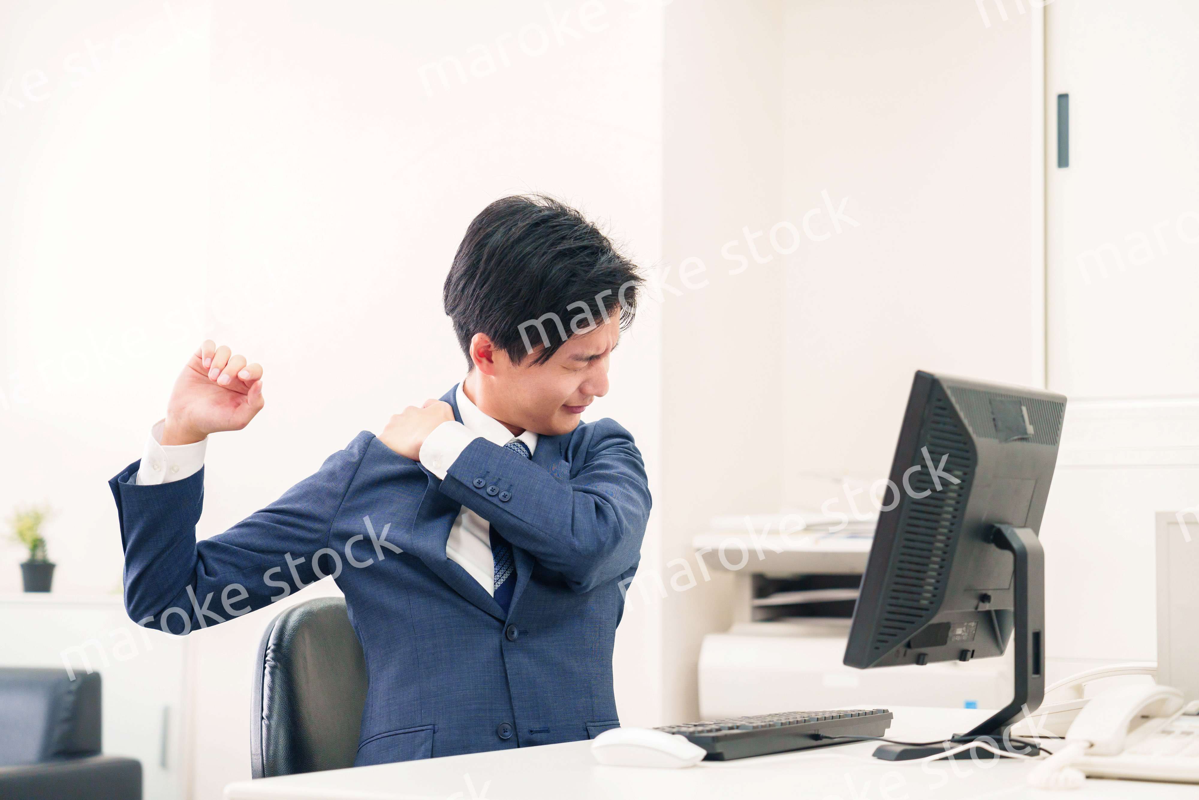 オフィスで肩こりに悩むビジネスマン