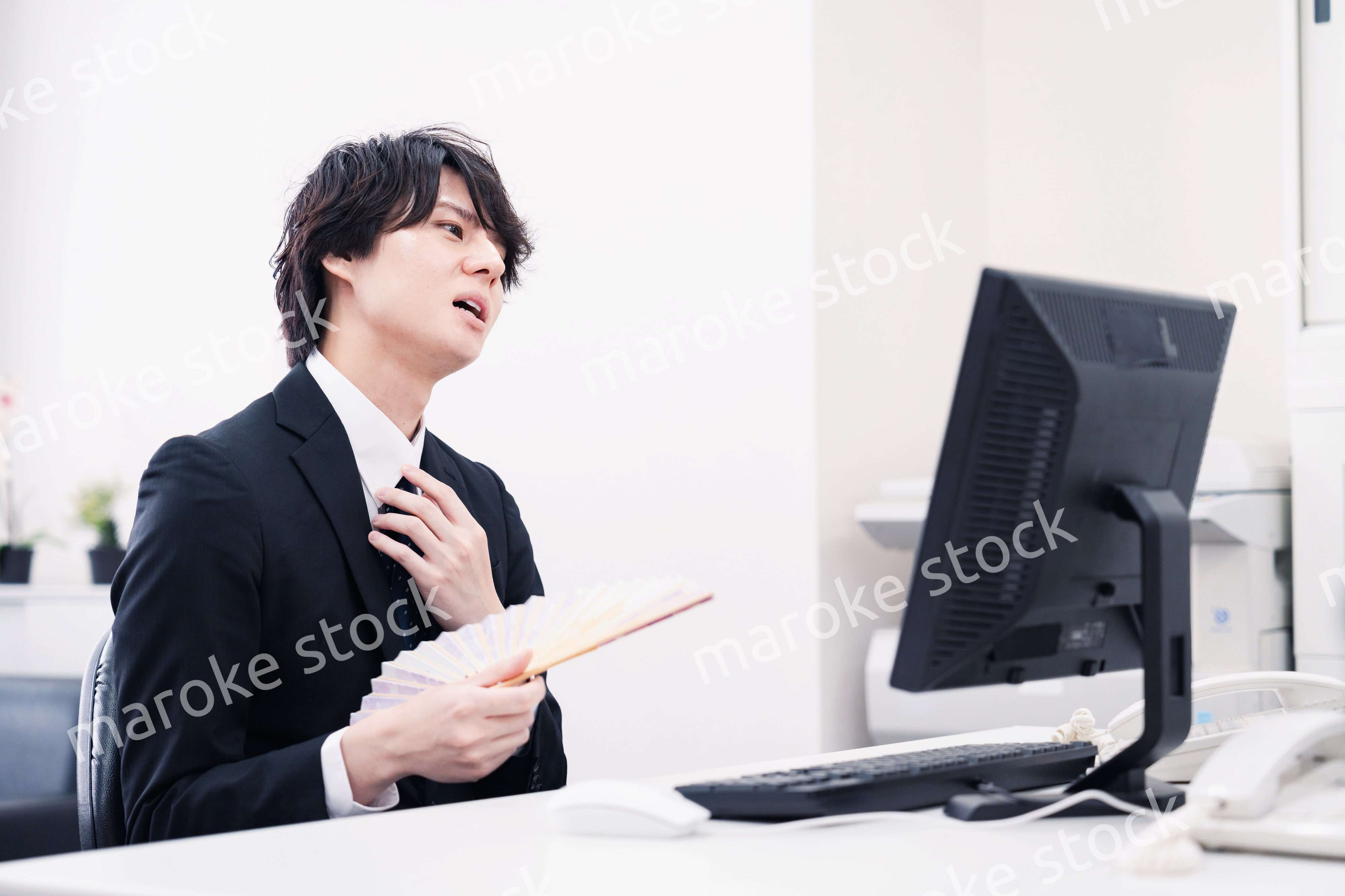 扇子で扇ぎながら仕事をするビジネスマン